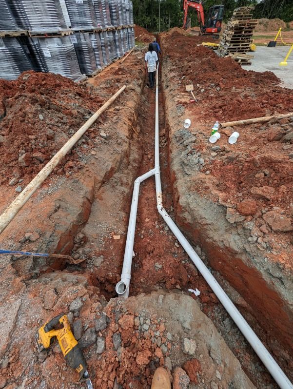 A construction site with a drill and pipes in the dirt.