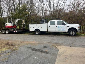 A white truck is parked next to a small excavator on a trailer.