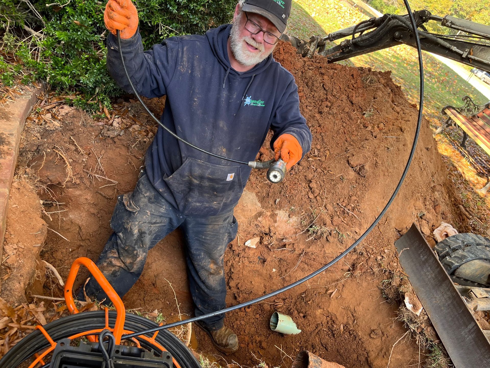 A man is kneeling in the dirt holding a hose.