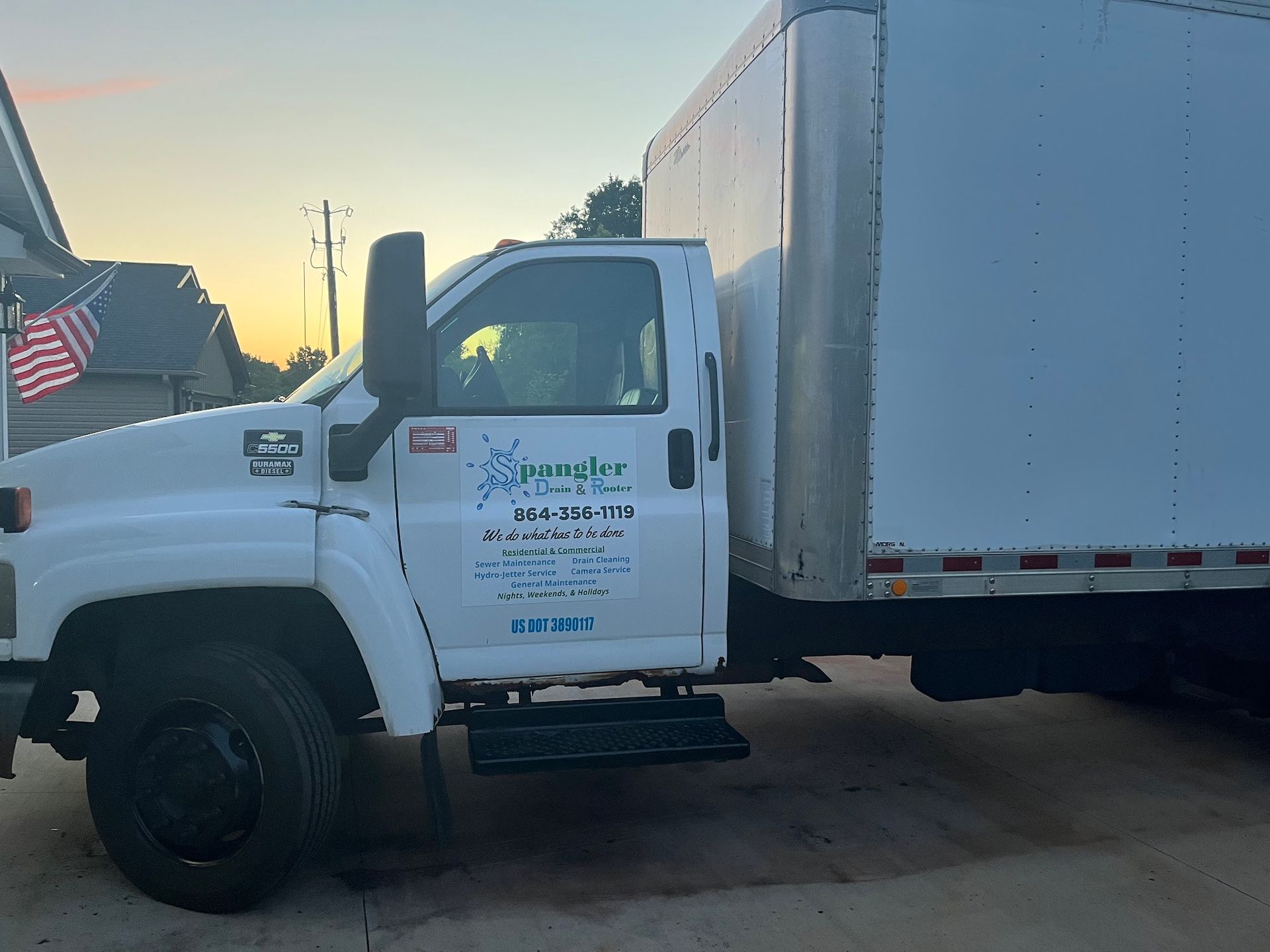 A white truck with a box on the back is parked in a driveway.