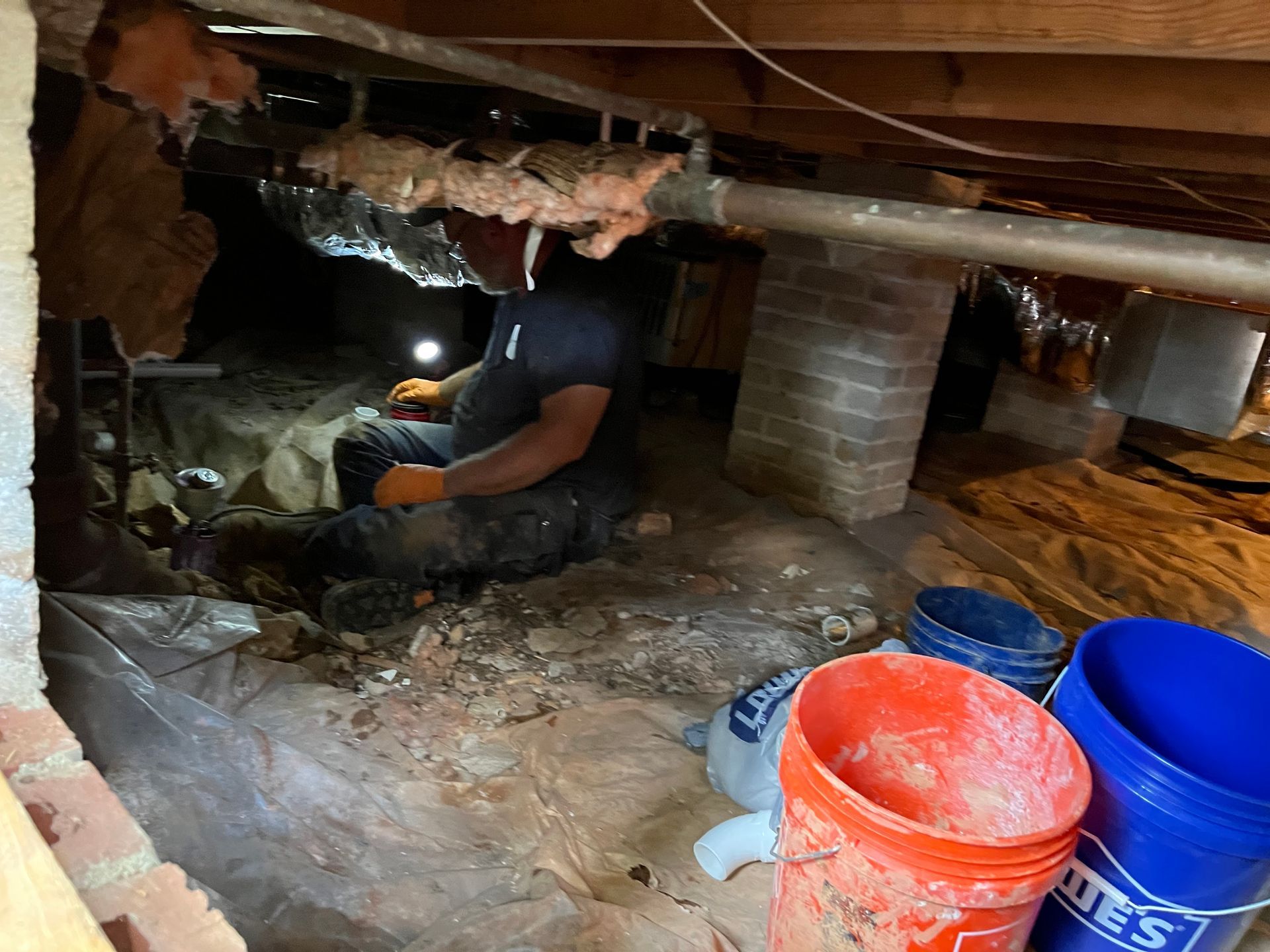 A man is kneeling down in a basement next to buckets.
