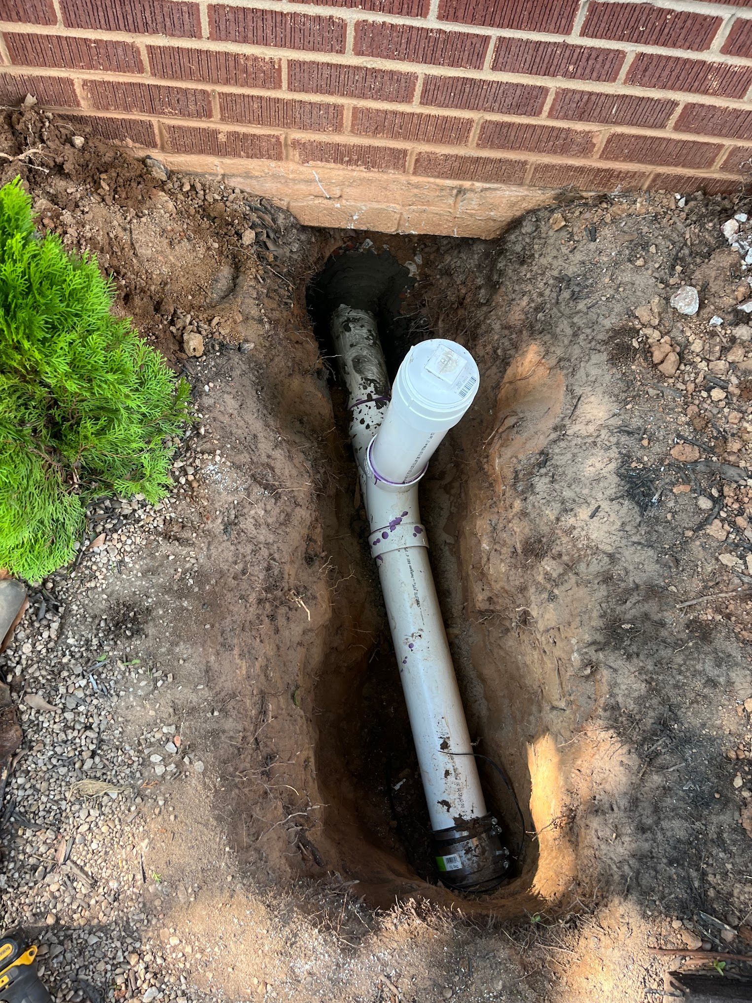 A white pipe is sitting in a hole in the ground next to a brick wall.
