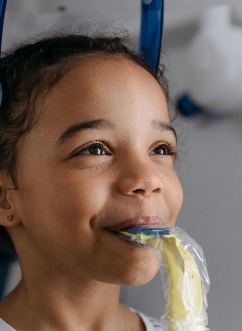 A little girl is eating a banana wrapped in plastic.