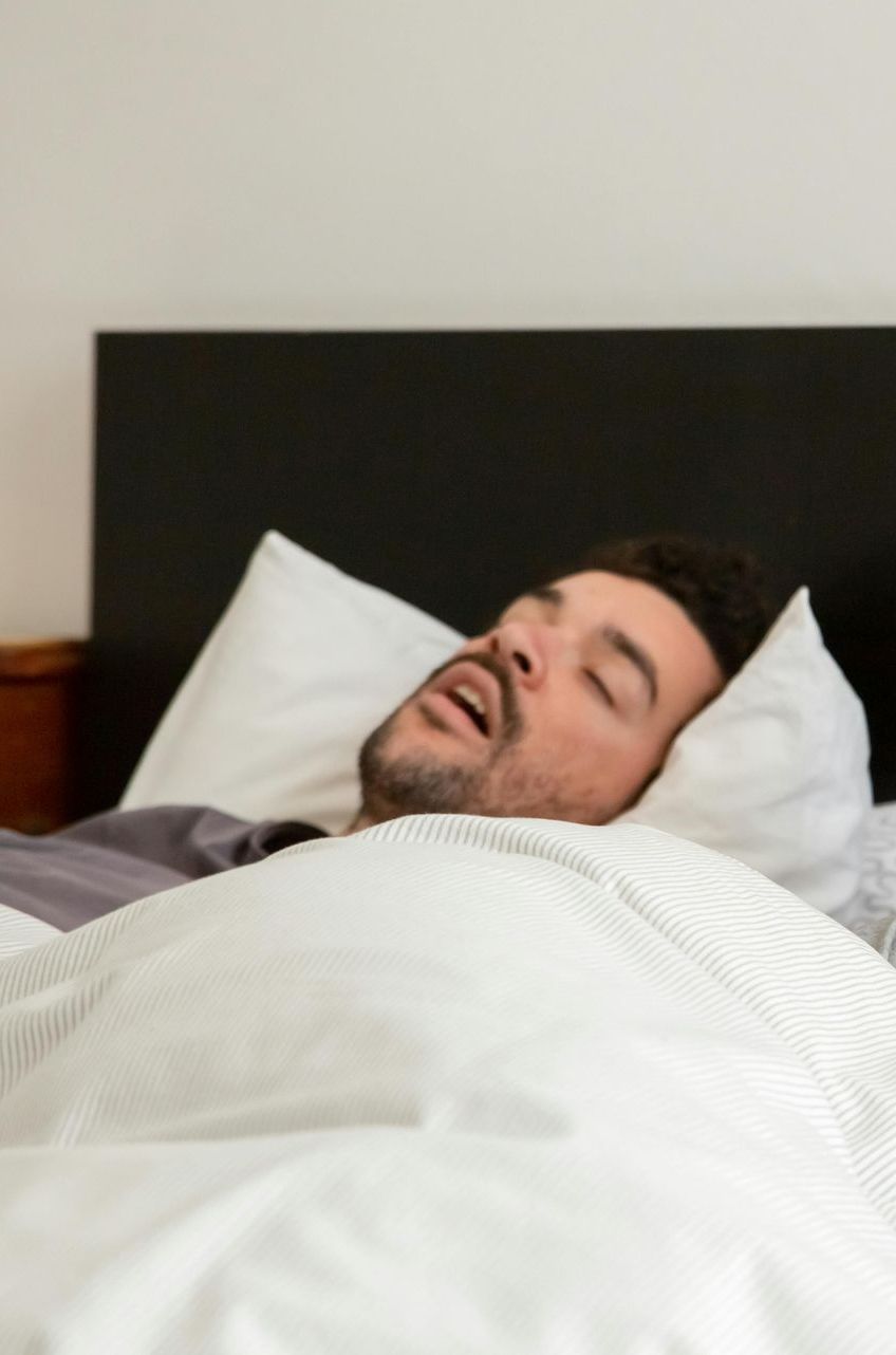 A man is sleeping in a bed with white sheets and pillows.