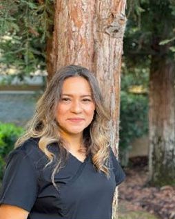 A woman in a black shirt is standing next to a tree.