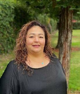 A woman in a black shirt is standing in front of a tree.