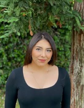 A woman in a black shirt is standing in front of a tree.