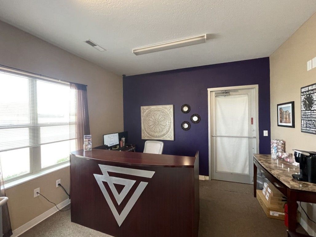 Reception desk in an office with a purple accent wall, art, and a waiting area.
