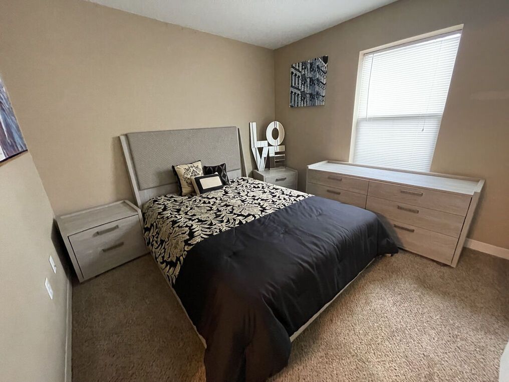 Bedroom with bed, nightstands, dresser, and window. Black and white bedding, neutral walls.