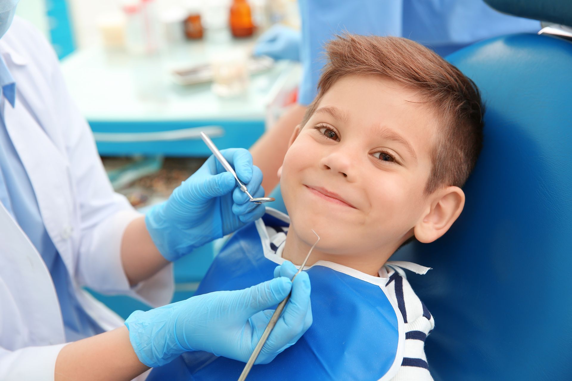 A young boy is sitting in a dental chair while a dentist examines his teeth.