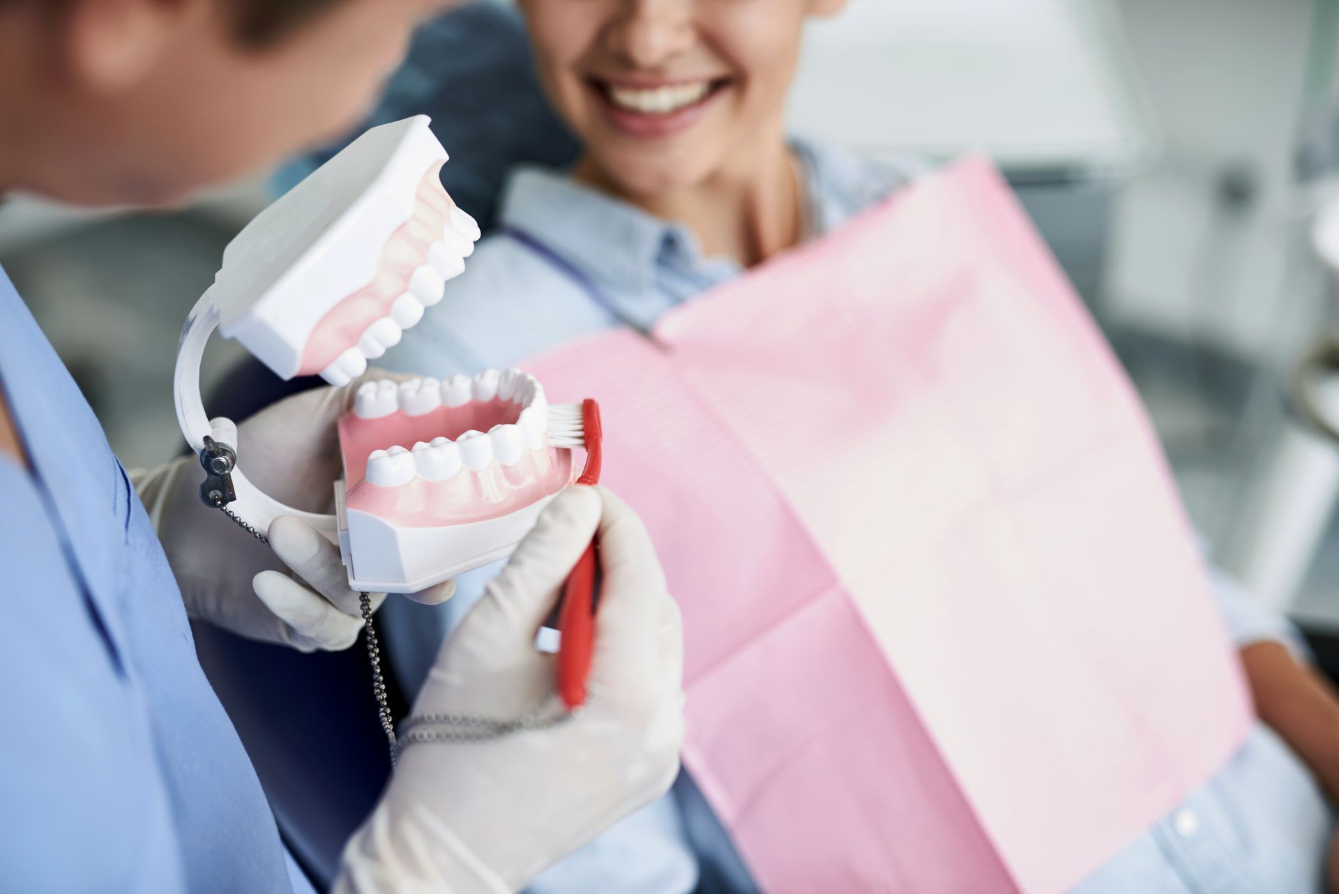 A dentist is showing a woman how to brush her teeth with a model of teeth.