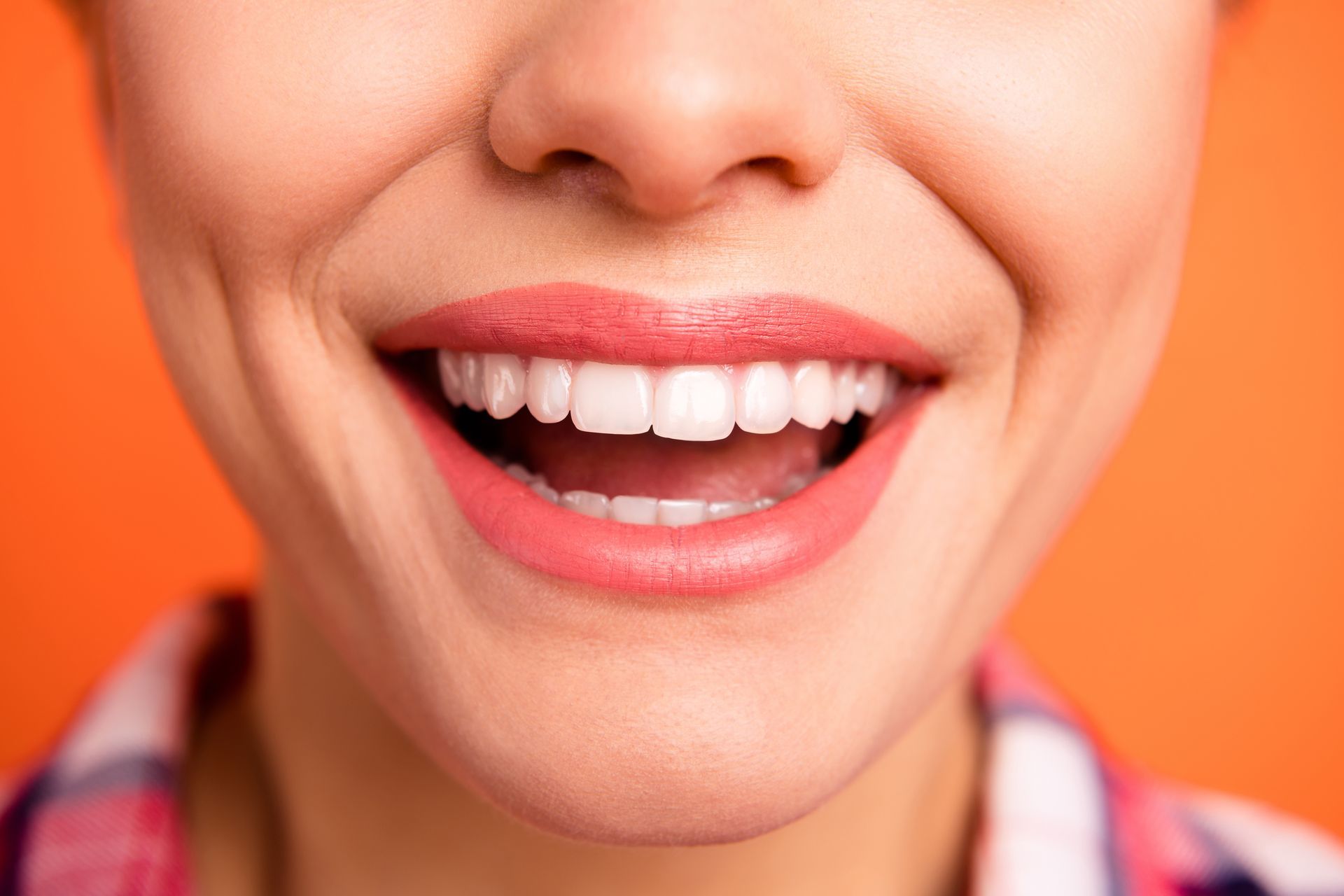 A close up of a woman 's mouth with white teeth and pink lipstick.