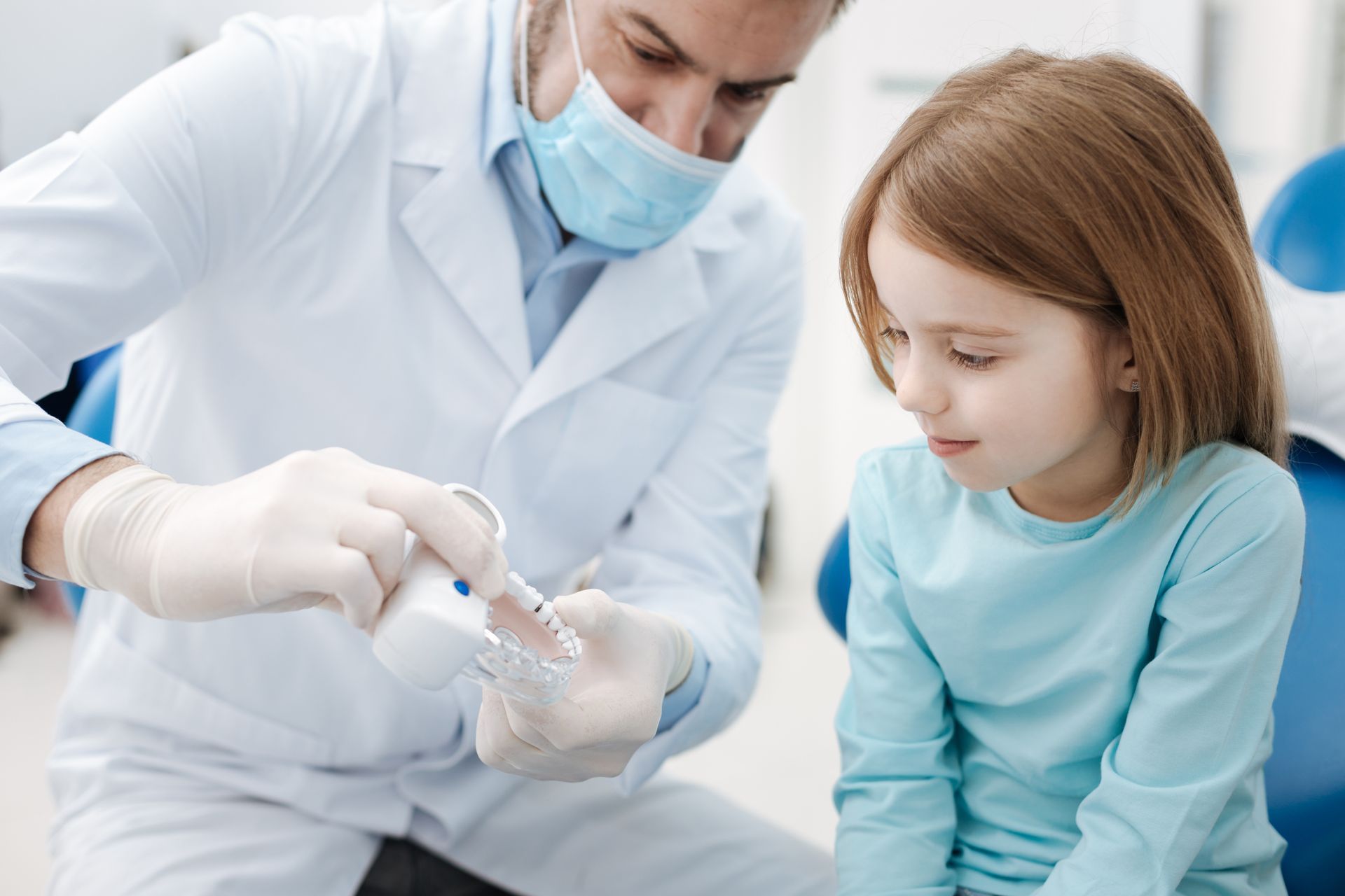 A little girl is sitting in a dental chair while a dentist examines her teeth.