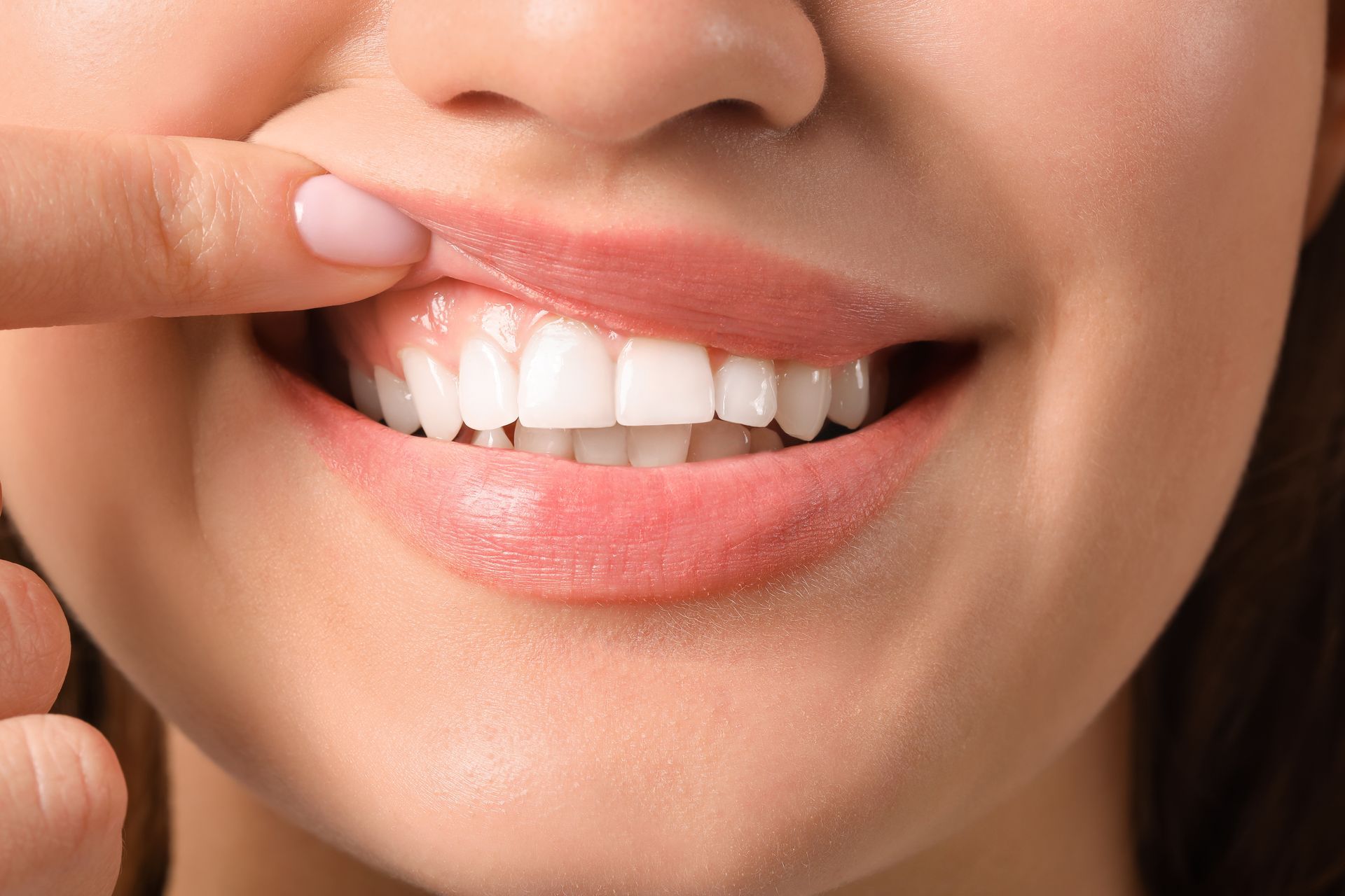 A woman is touching her teeth with her finger.