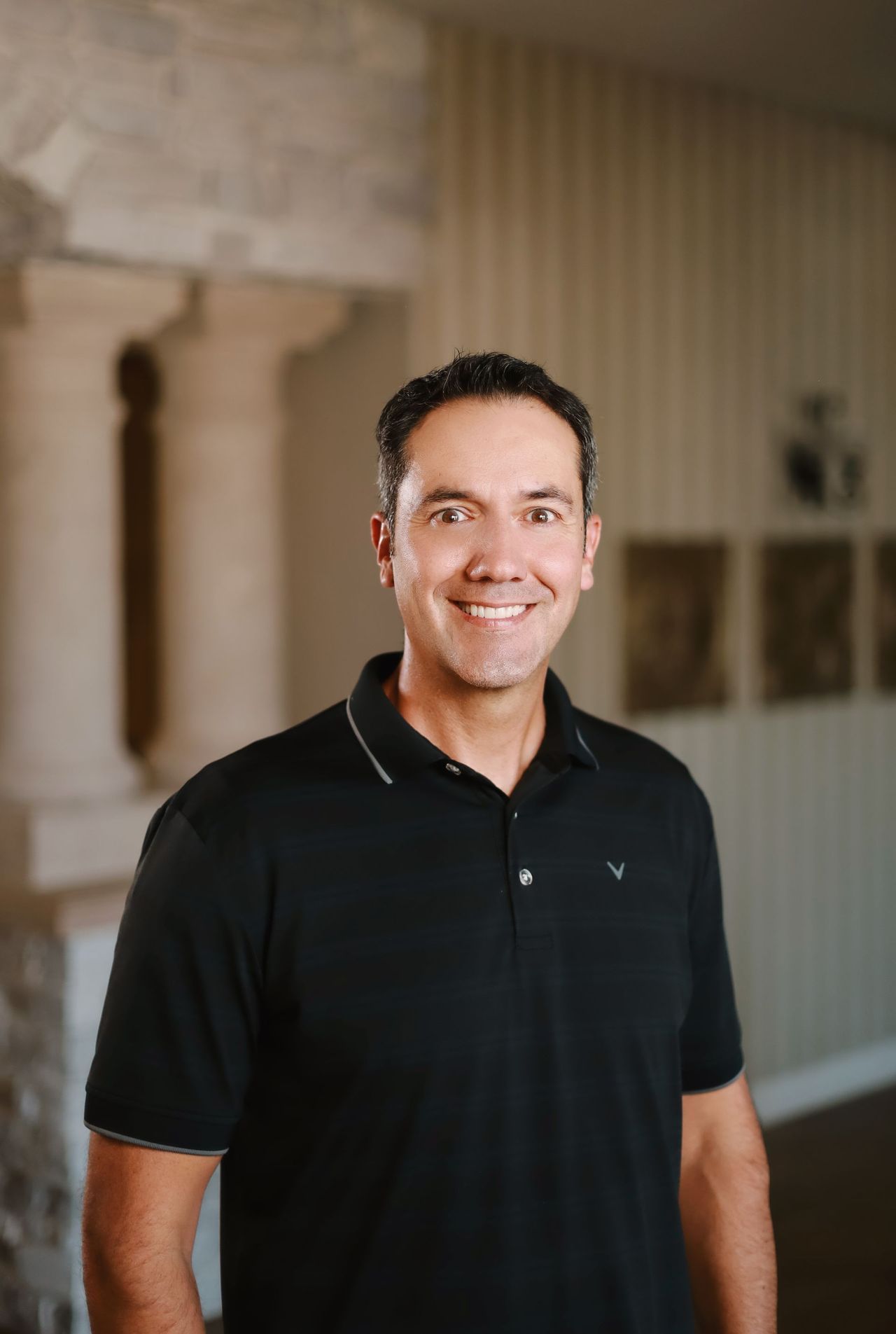 A man in a black polo shirt is smiling for the camera.