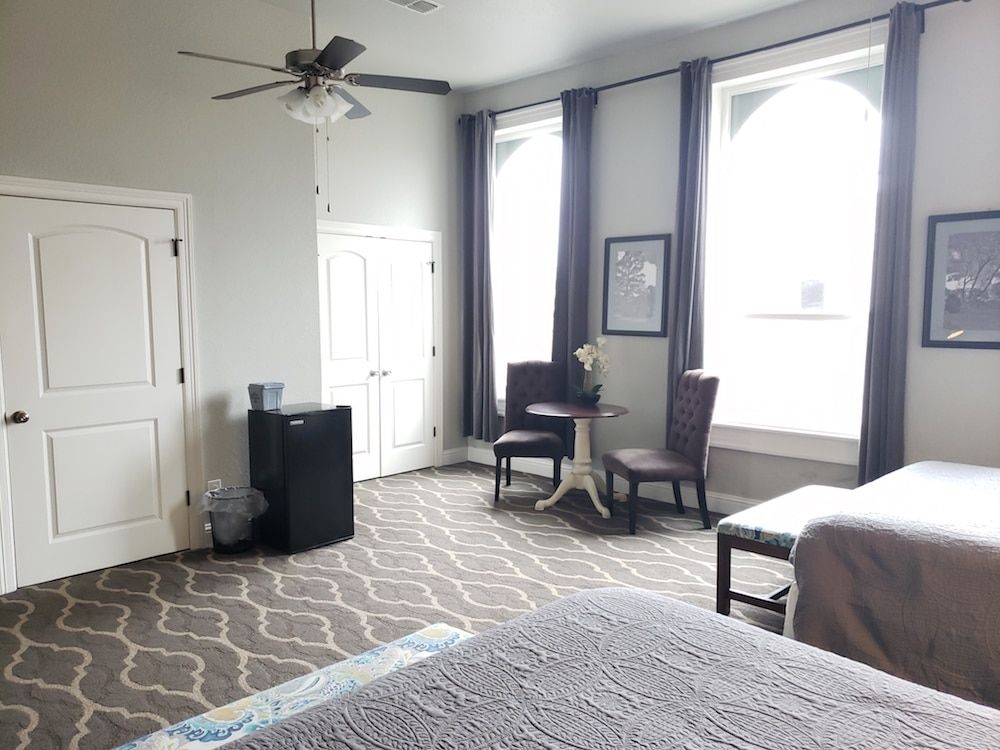 A hotel room with two beds , a table , chairs and a ceiling fan.