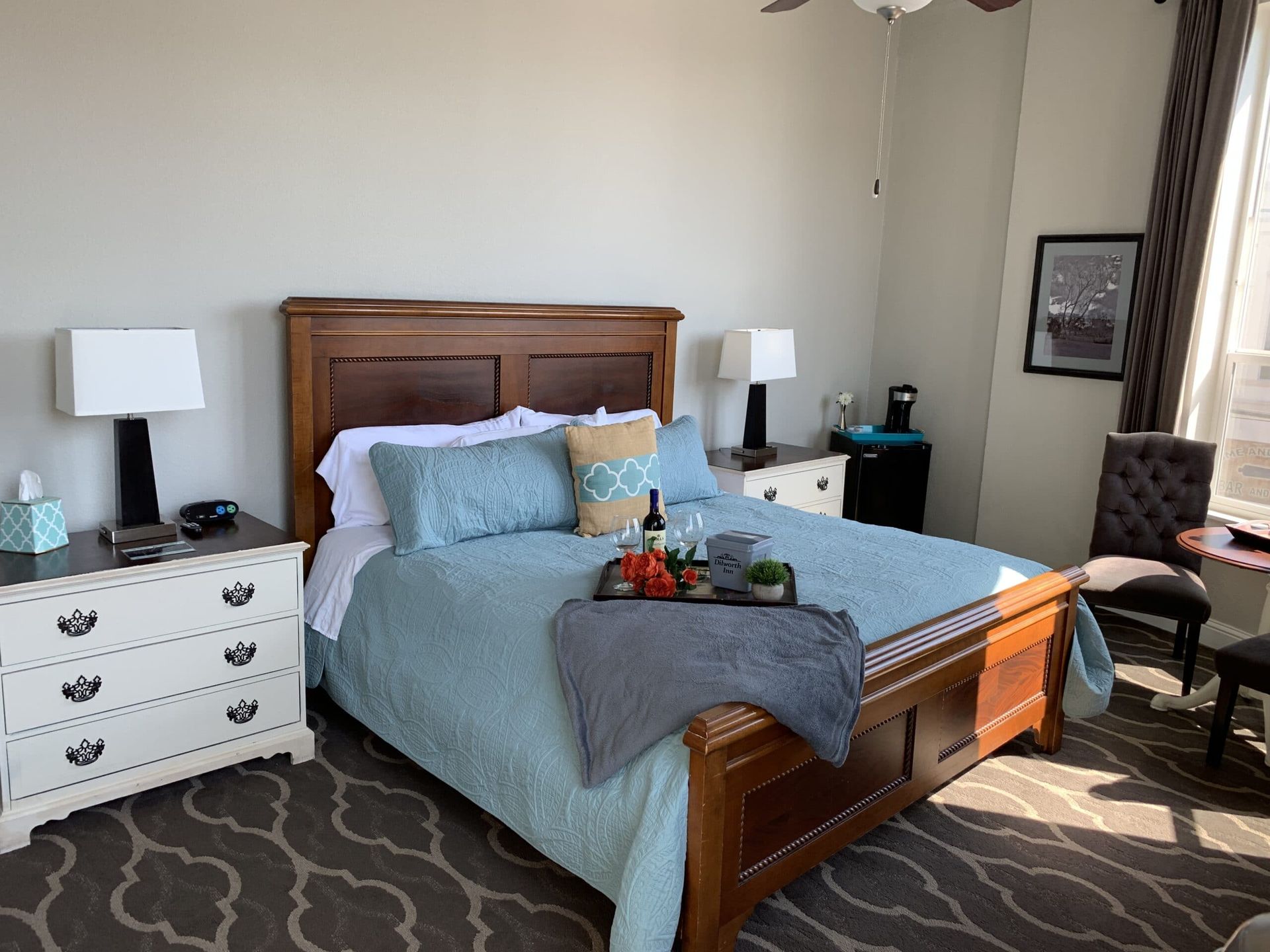 A bedroom with a bed , dresser , chair , table and window.
