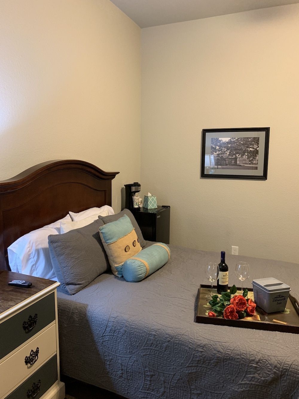 A bedroom with a bed , dresser , nightstand and a tray with a bottle of wine on it.