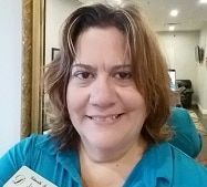 A woman in a blue shirt is smiling and holding a name tag.
