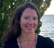 A woman is smiling in front of a body of water.