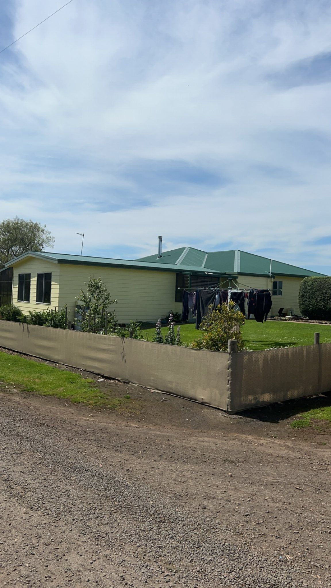 Yellow house with green roof, behind a concrete wall, against a blue sky.