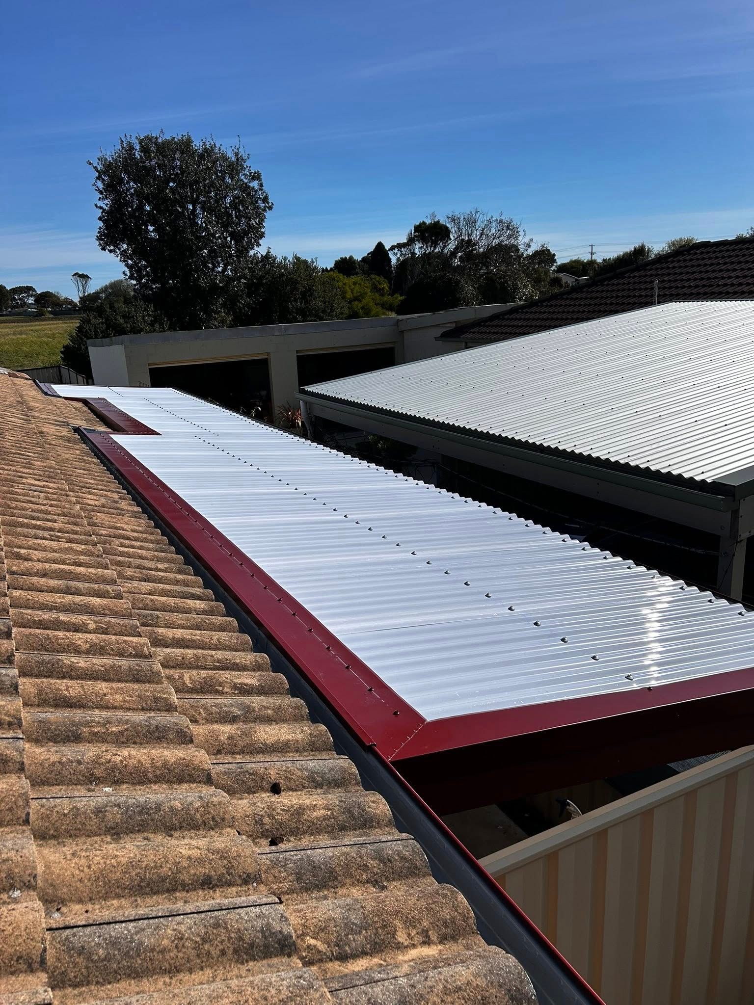 A rooftop with new corrugated roofing installed over a red frame, against a blue sky.