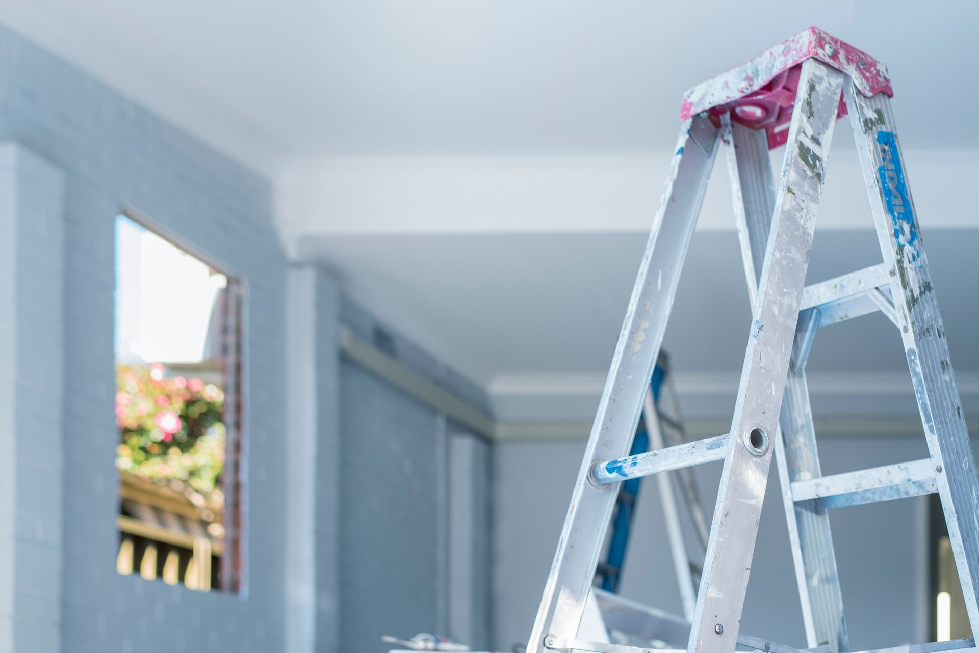 Ladder in a room under construction, with a partially visible window and light blue walls.