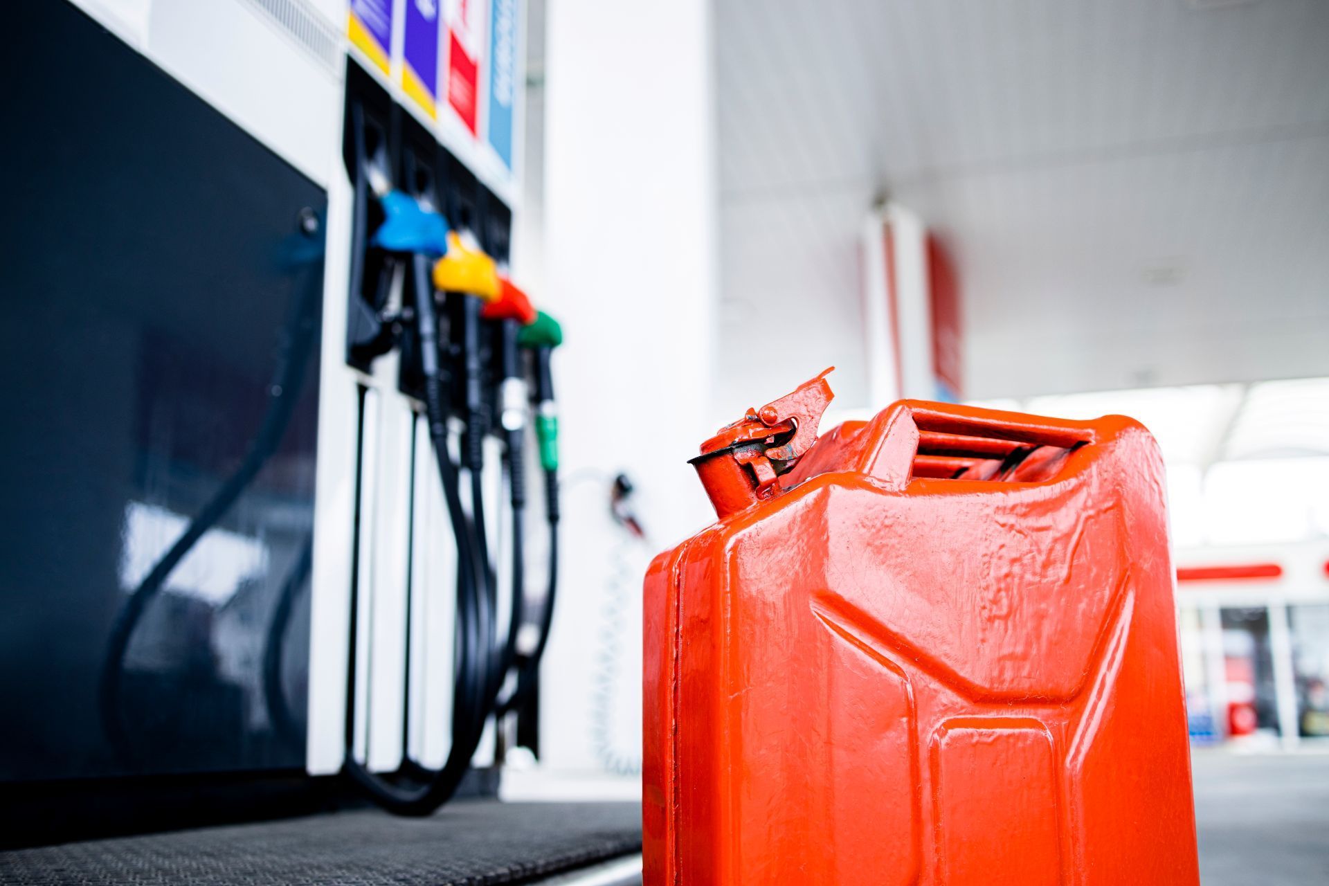 Orange gas can at a gas station with fuel nozzles in the background.