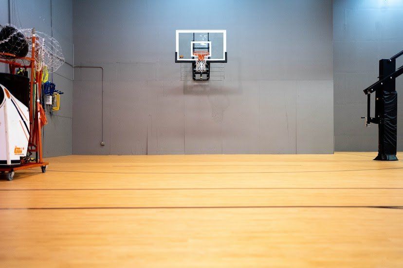 Basketball hoop on gray wall in an indoor court; wooden floor, equipment on left.