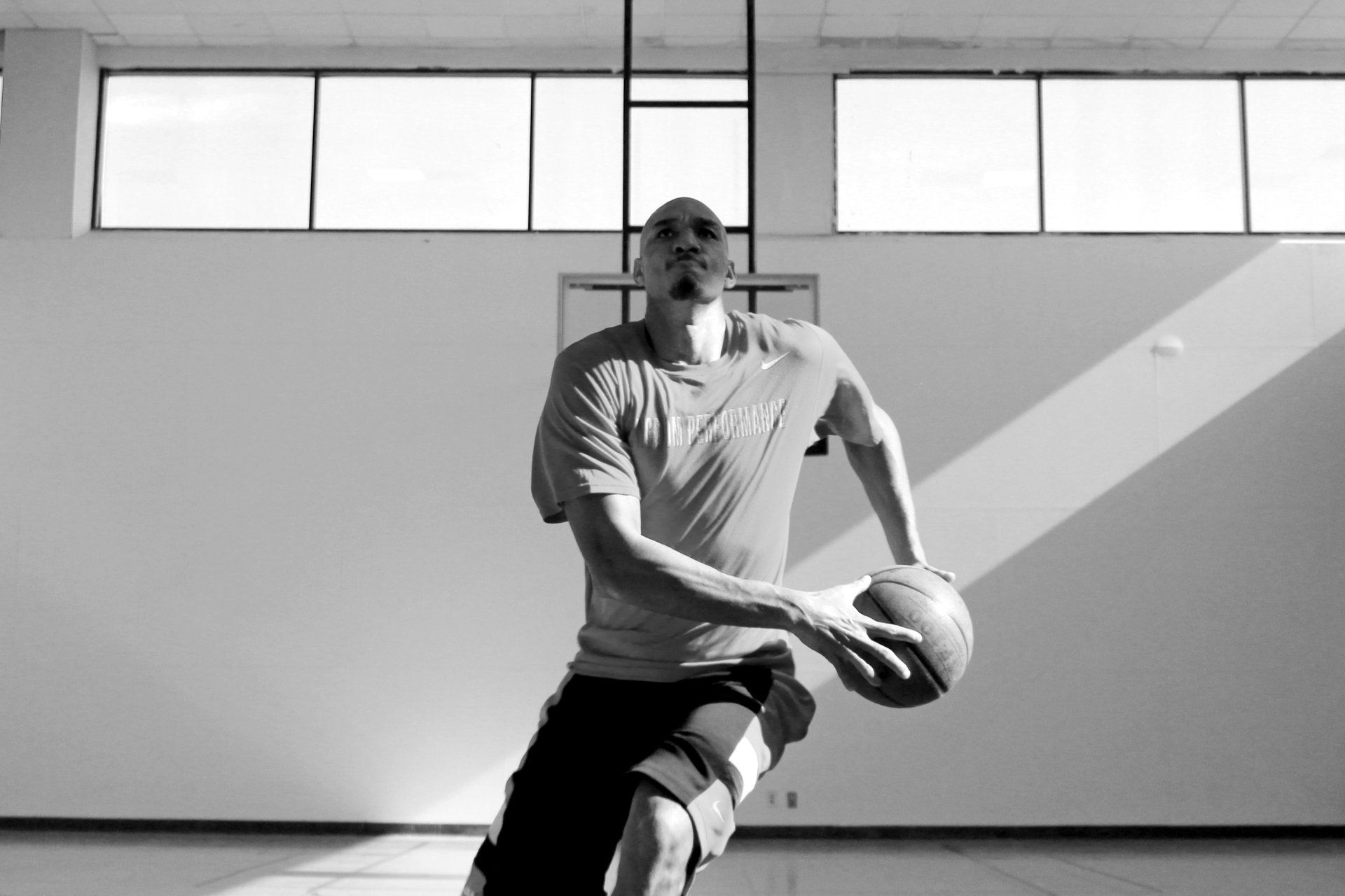Basketball player dribbling, wearing a tee and shorts in a gym.
