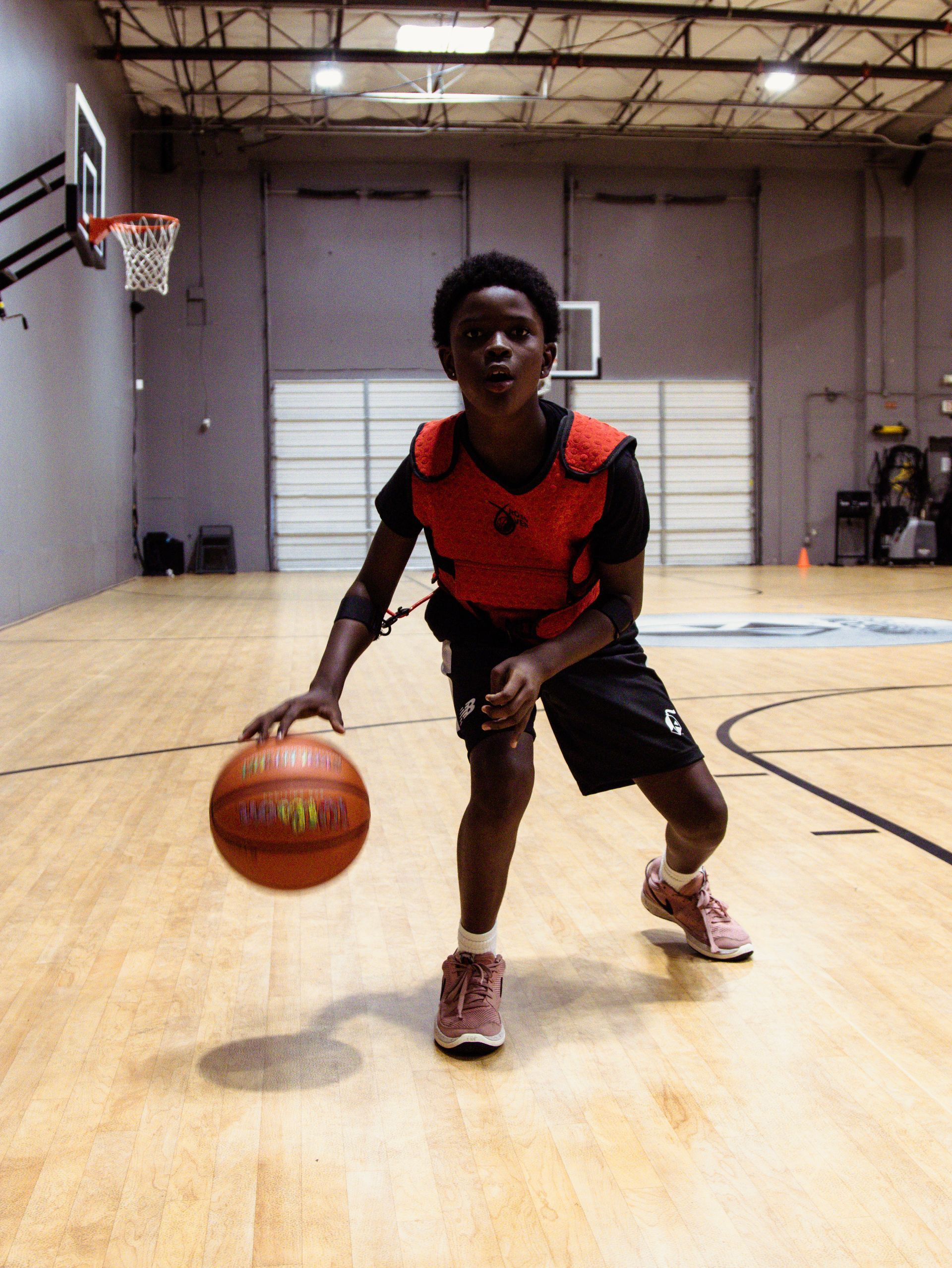 Young basketball player dribbling a ball on a court, wearing a training vest, eyes focused.