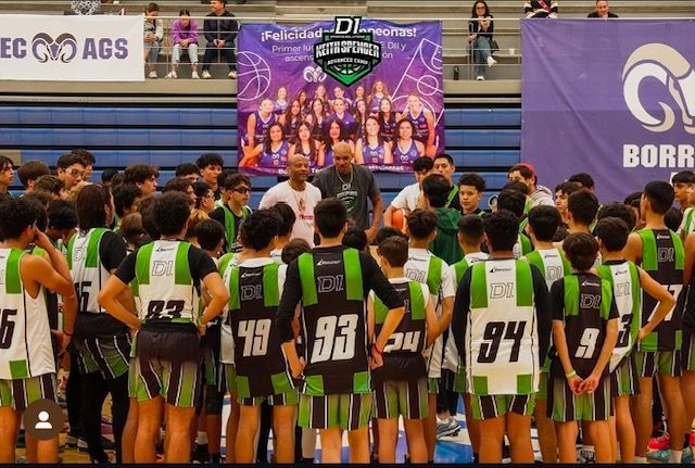 Basketball team huddle with coach on court, wearing green and black jerseys, banner in background.
