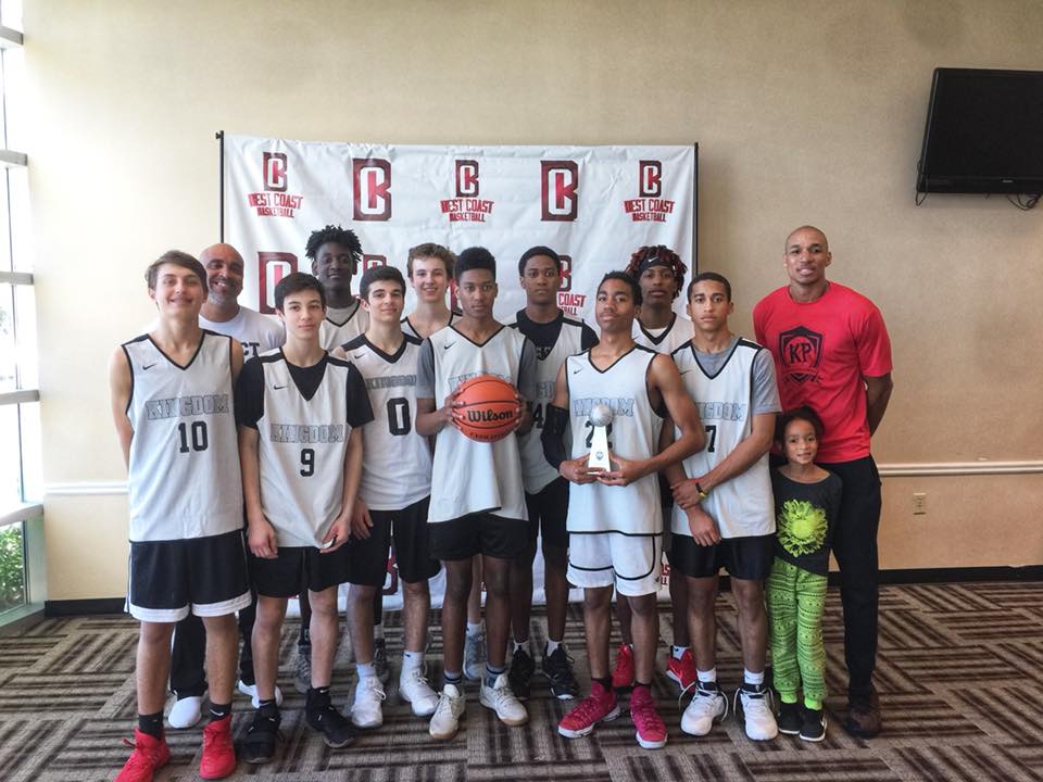 Basketball team poses with trophy; grey jerseys, black shorts, indoors.