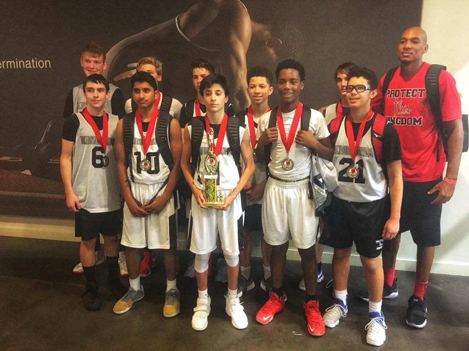 Basketball team posing with medals and trophy; indoors. Players are wearing black and white uniforms.