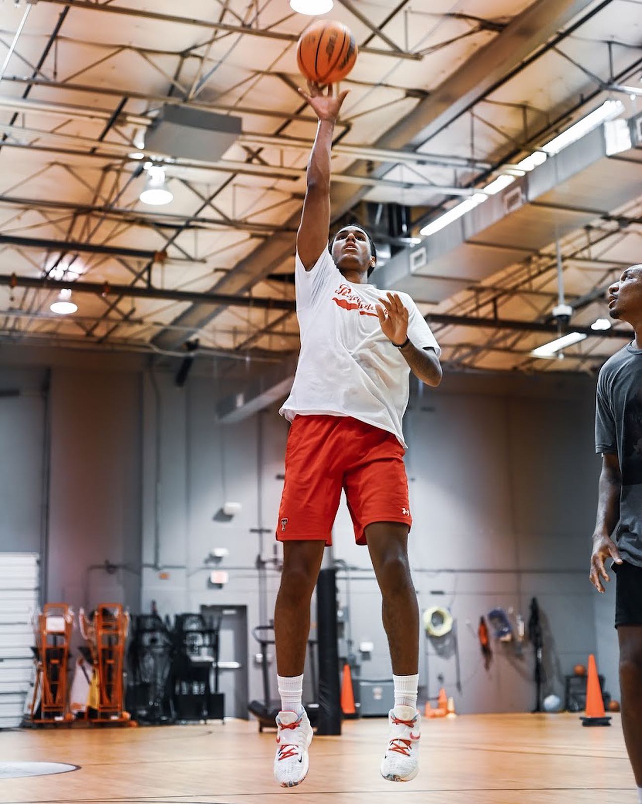 Basketball player in red shorts shooting a jump shot indoors, orange ball.