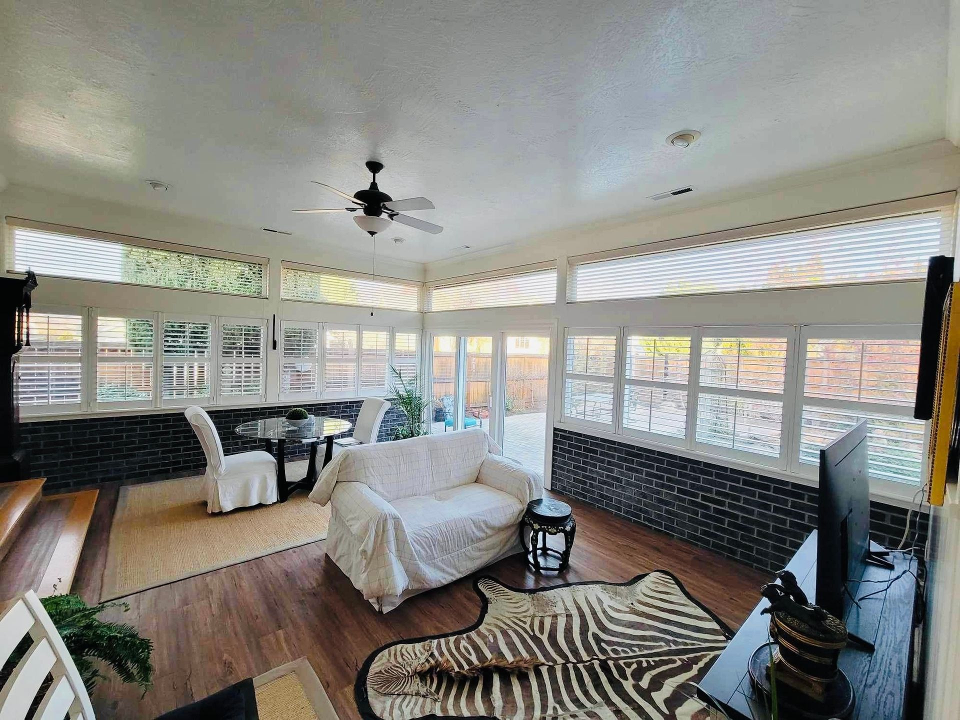 A sunroom with windows, a white sofa, a zebra-print rug, a dining table, and a dark accent wall.