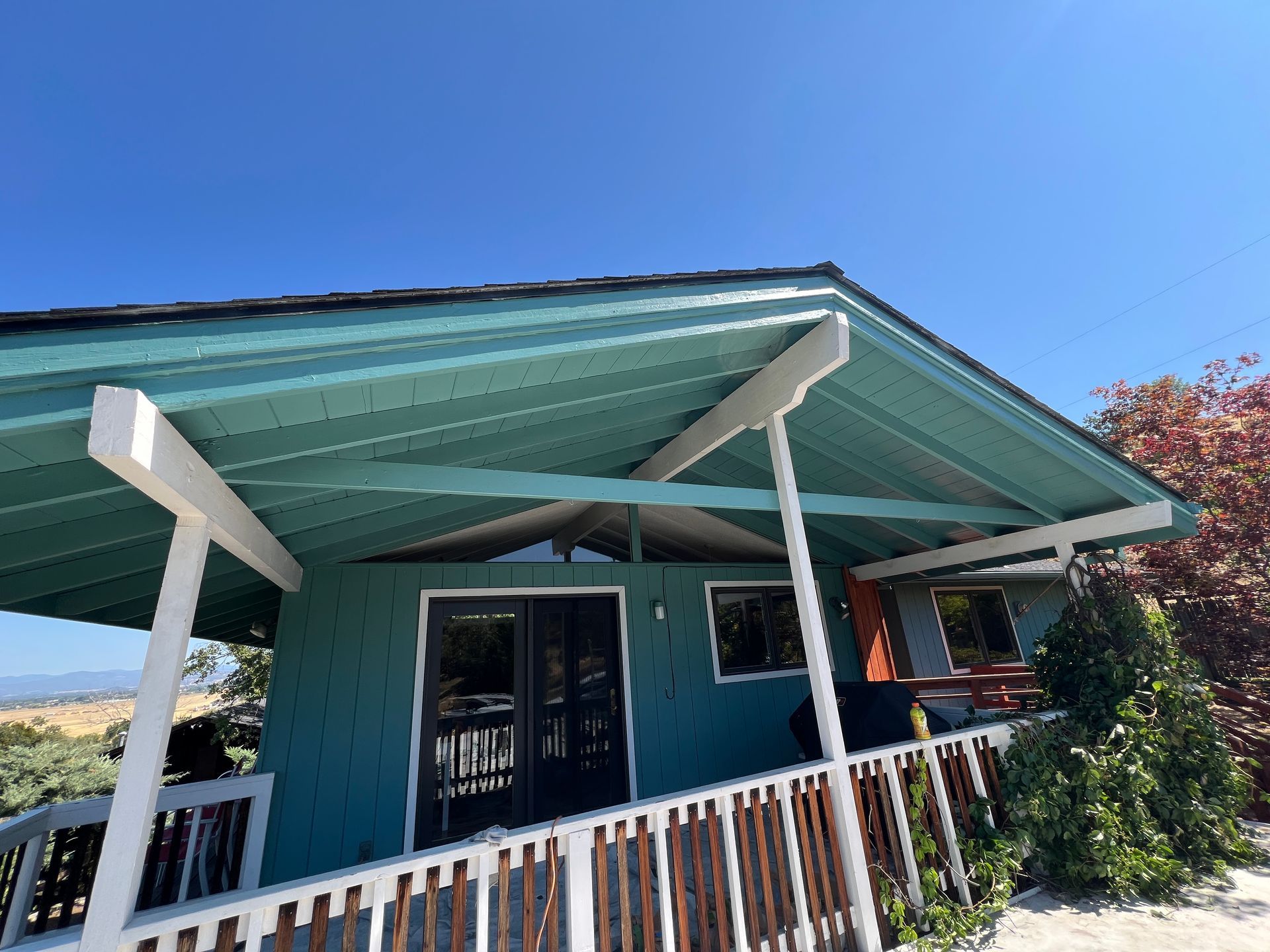 A teal house with a wooden deck and white railings under a clear blue sky.