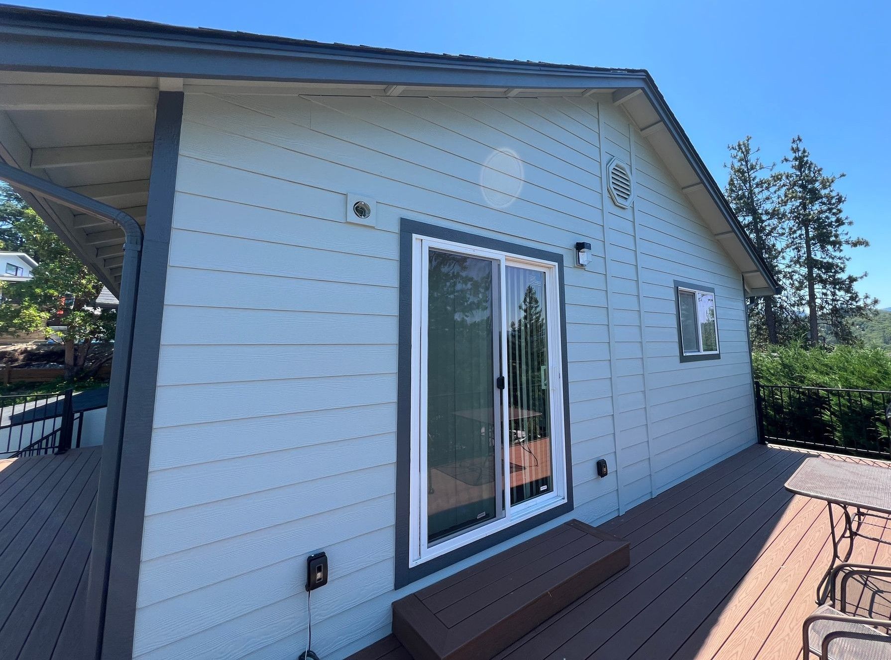 A blue-sided home with a sliding glass door and a wooden deck under a bright blue sky.
