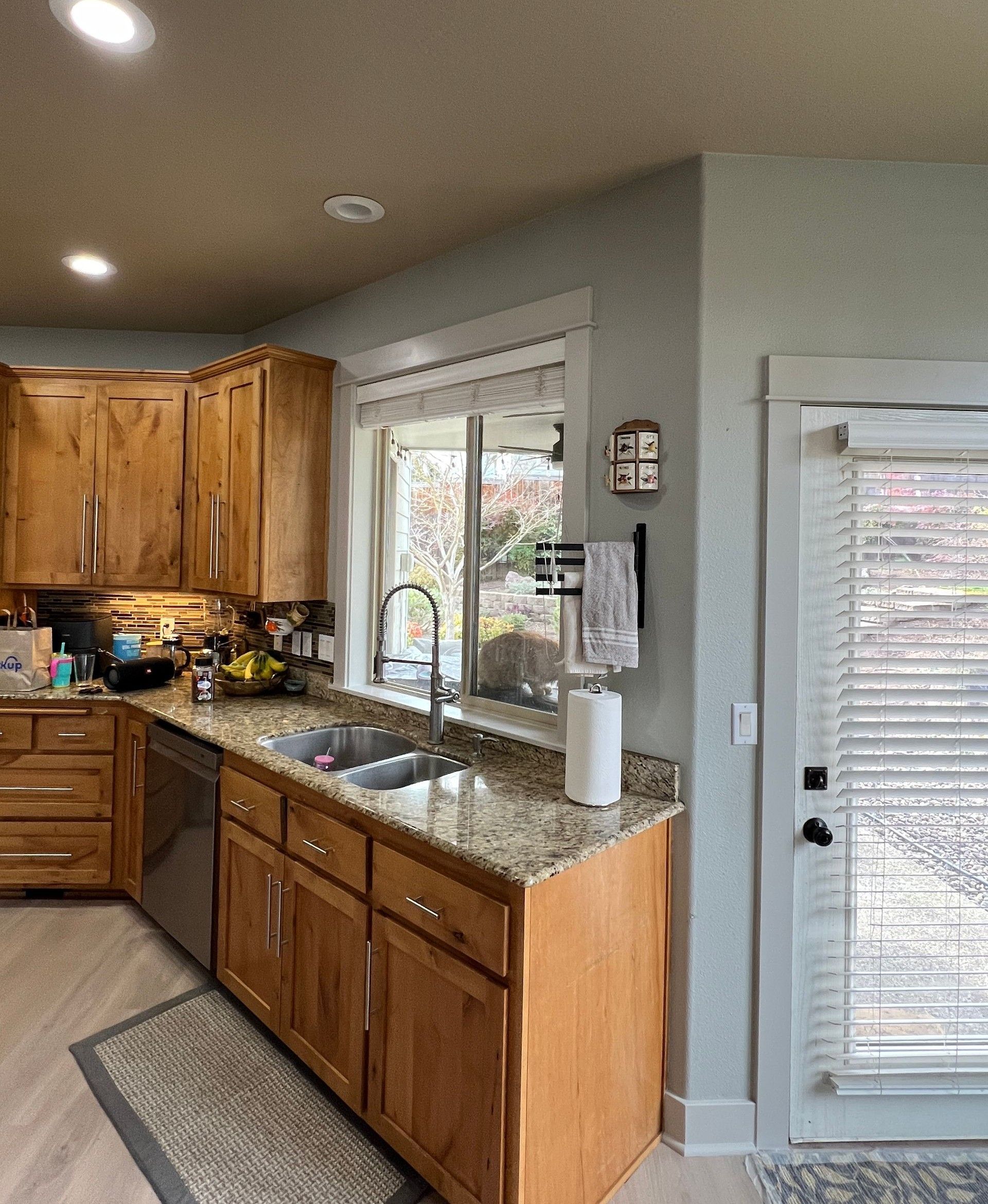 A kitchen with wooden cabinets, granite countertops, a stainless steel sink, and an adjacent door leading to the outside.