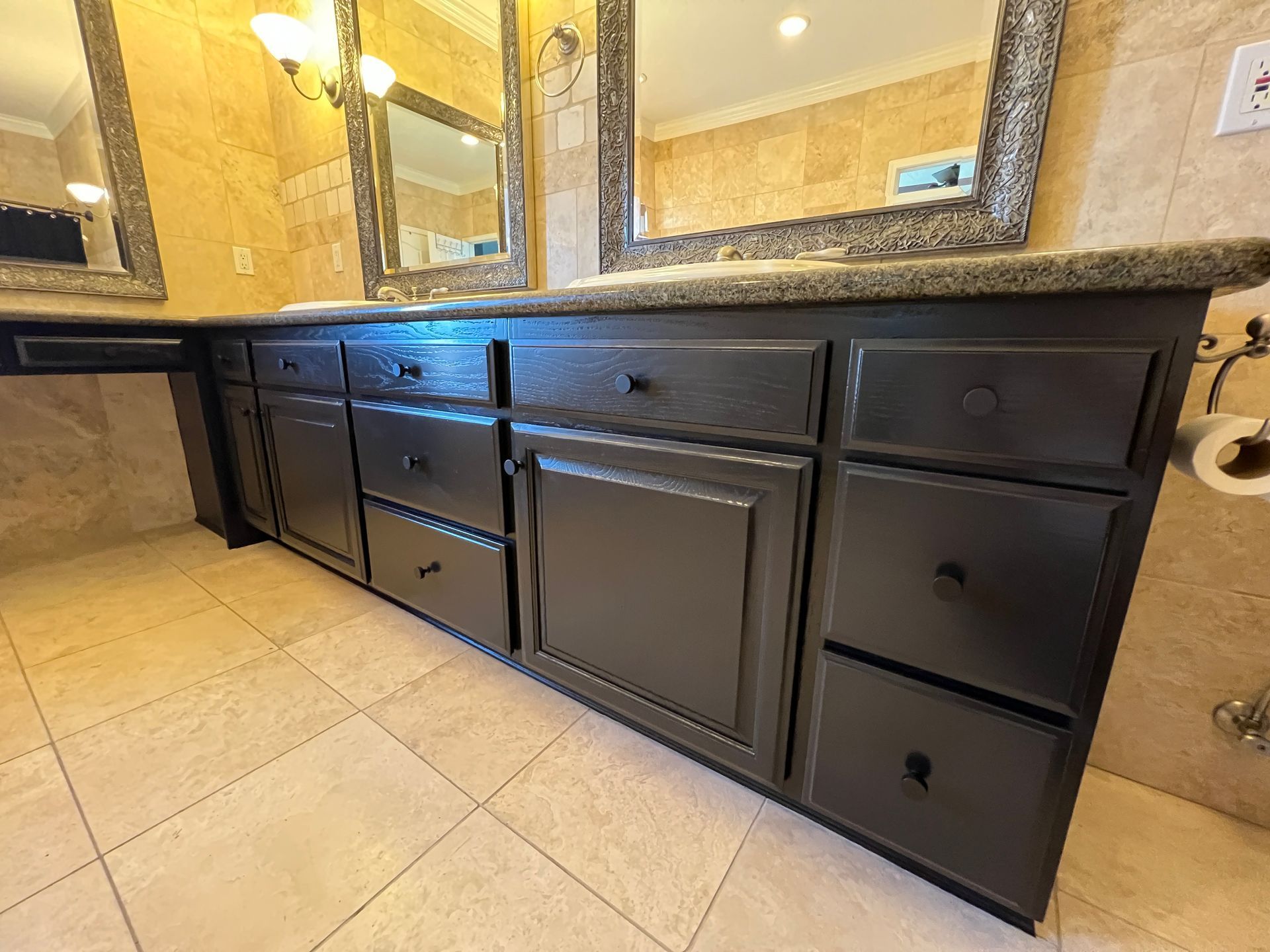 A bathroom vanity with dark painted cabinets and stone countertops, positioned beneath two framed mirrors.