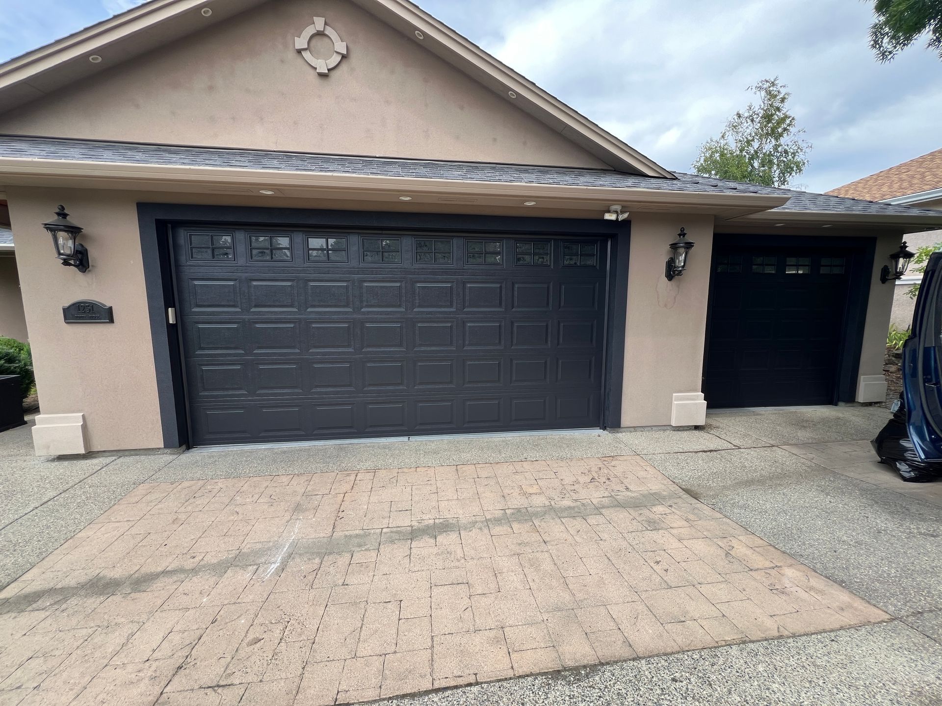 A beige house exterior featuring a large, dark gray two-car garage door and a smaller, adjacent single garage door.