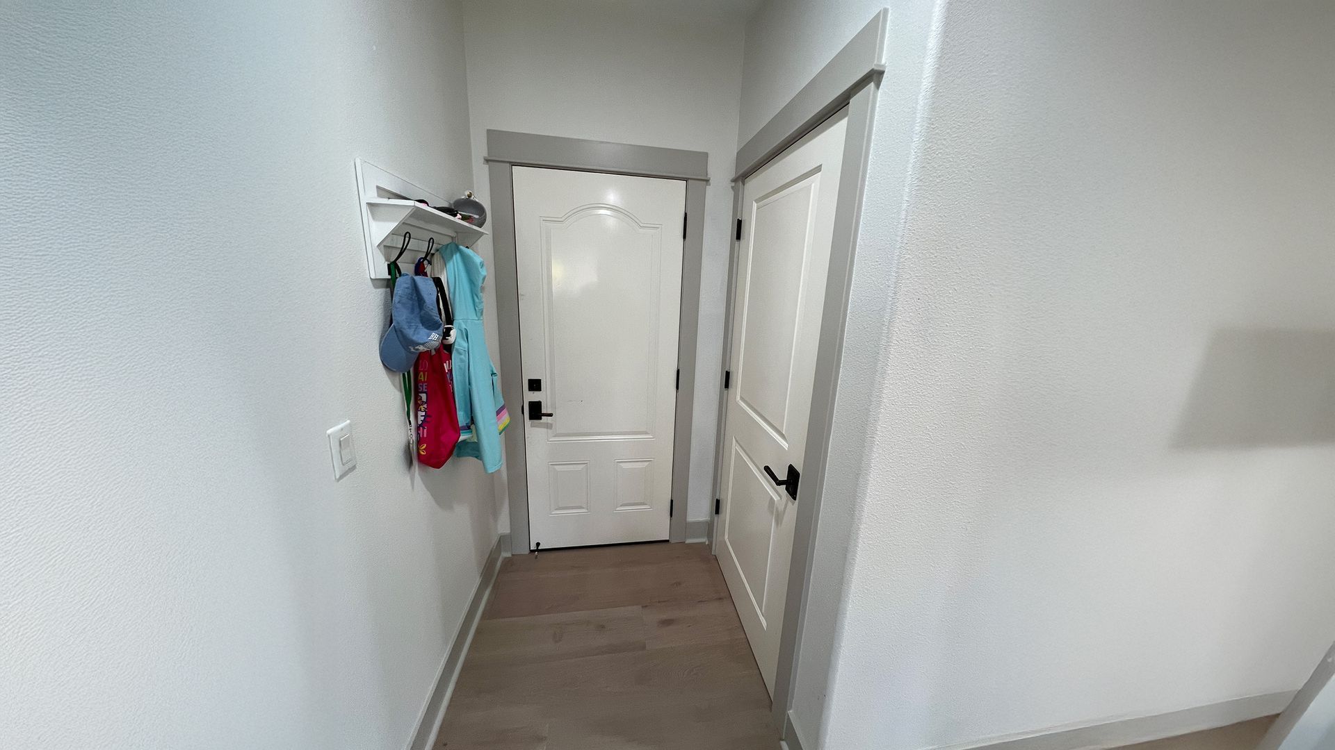 An entryway with a white front door, a closed interior door, and a wall-mounted rack holding coats and bags.