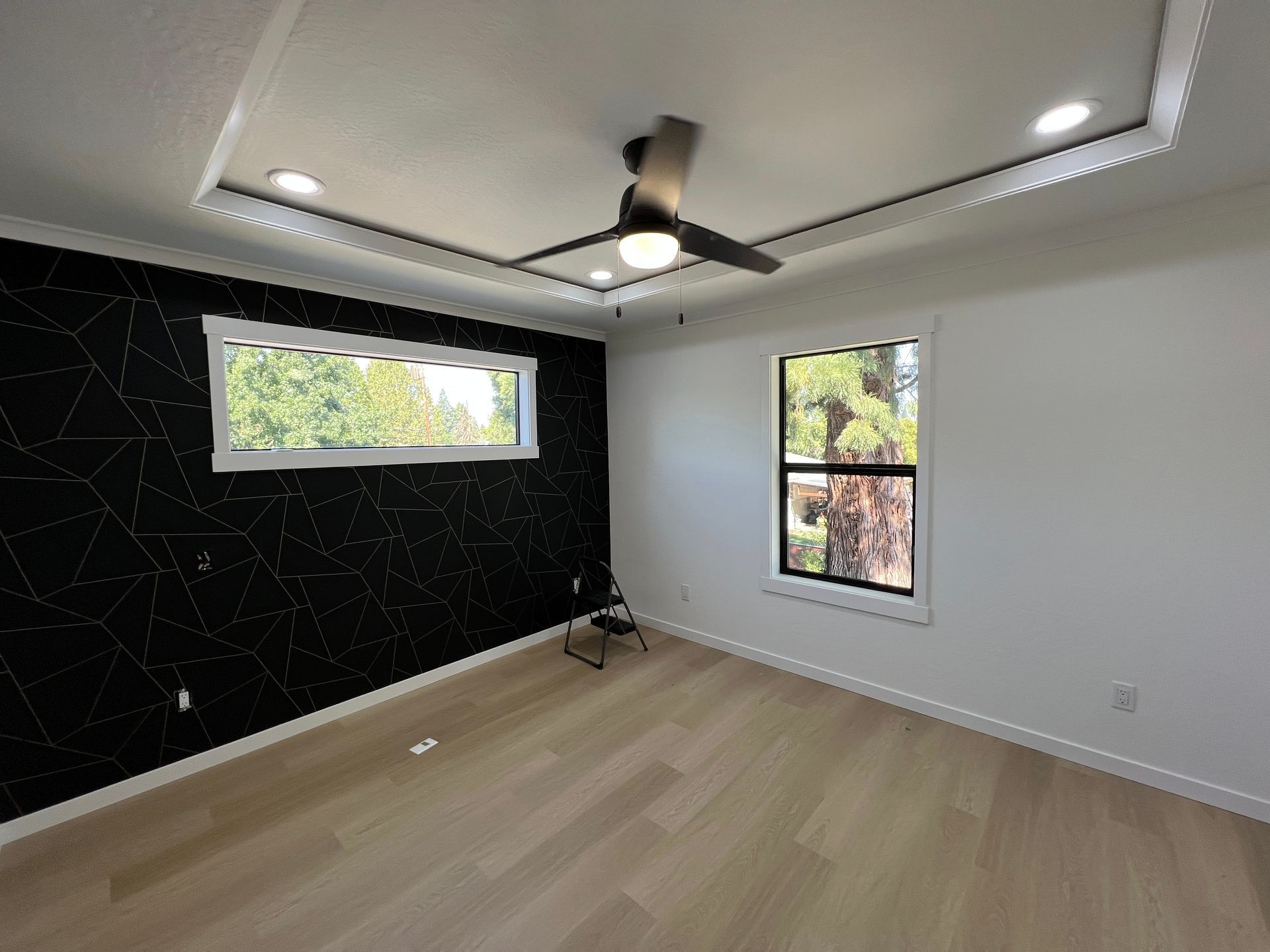 A minimalist bedroom with light wood floors, white walls, and a black accent wall featuring a geometric white pattern.