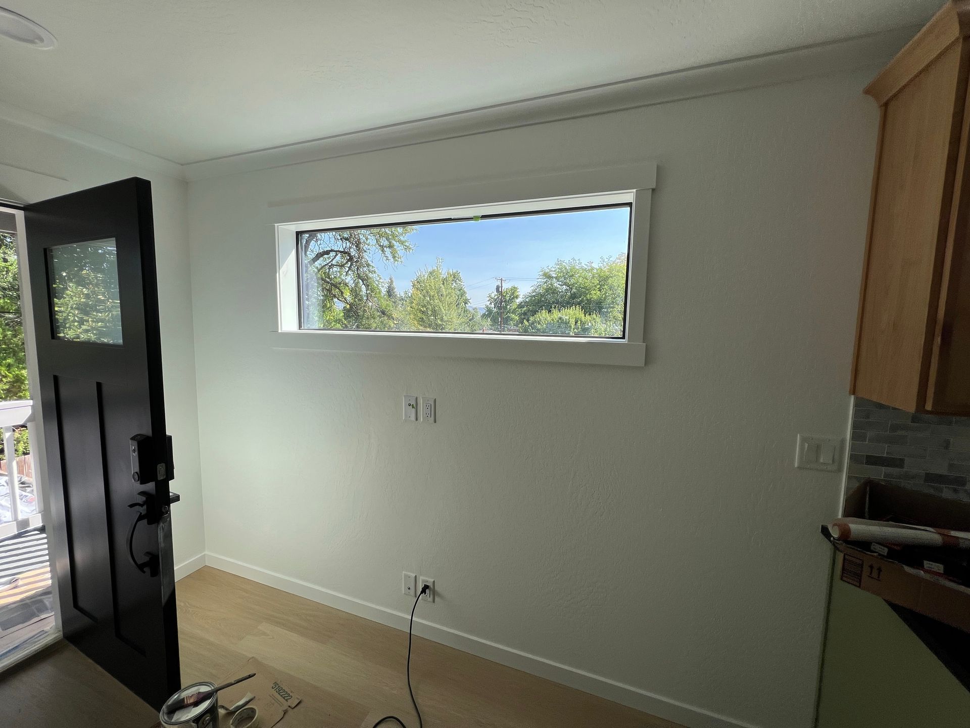 A horizontal window is centered on a white wall next to a black door in a room with light-colored flooring.