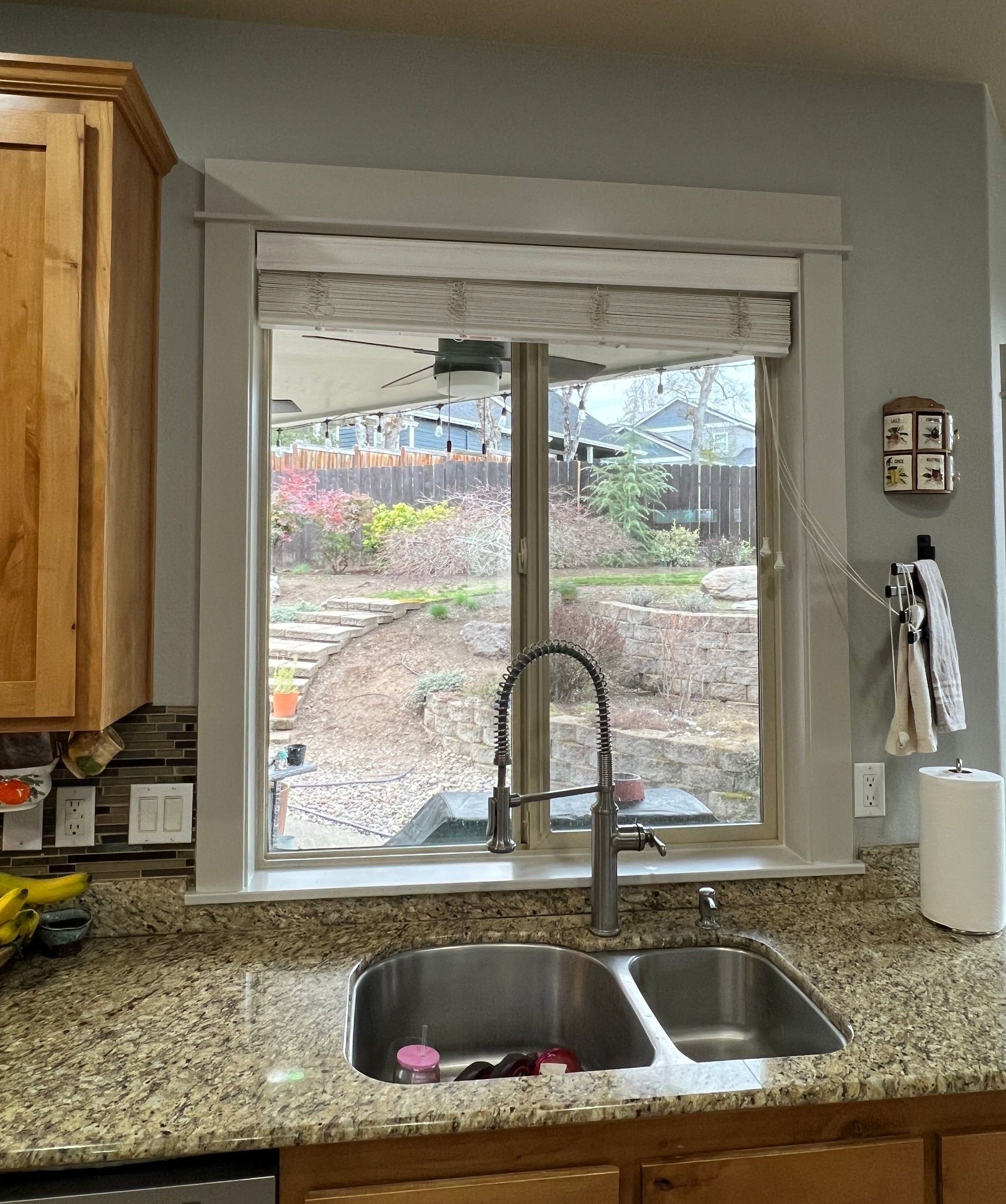 Kitchen sink with a tall metal faucet, granite countertops, and a window looking out onto a landscaped backyard.