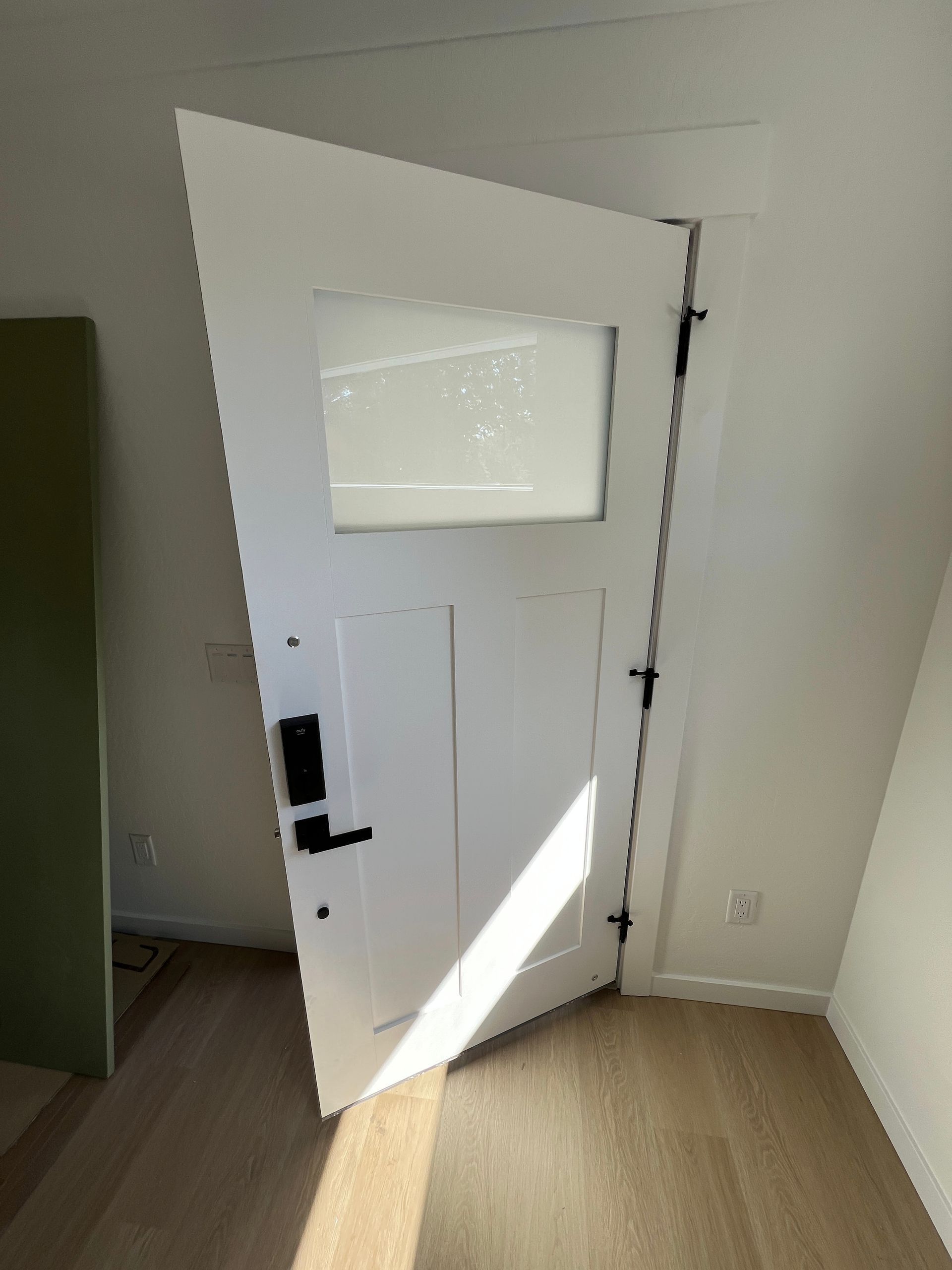 A white door with a glass window pane stands slightly ajar in a room with light wooden floors and white walls.