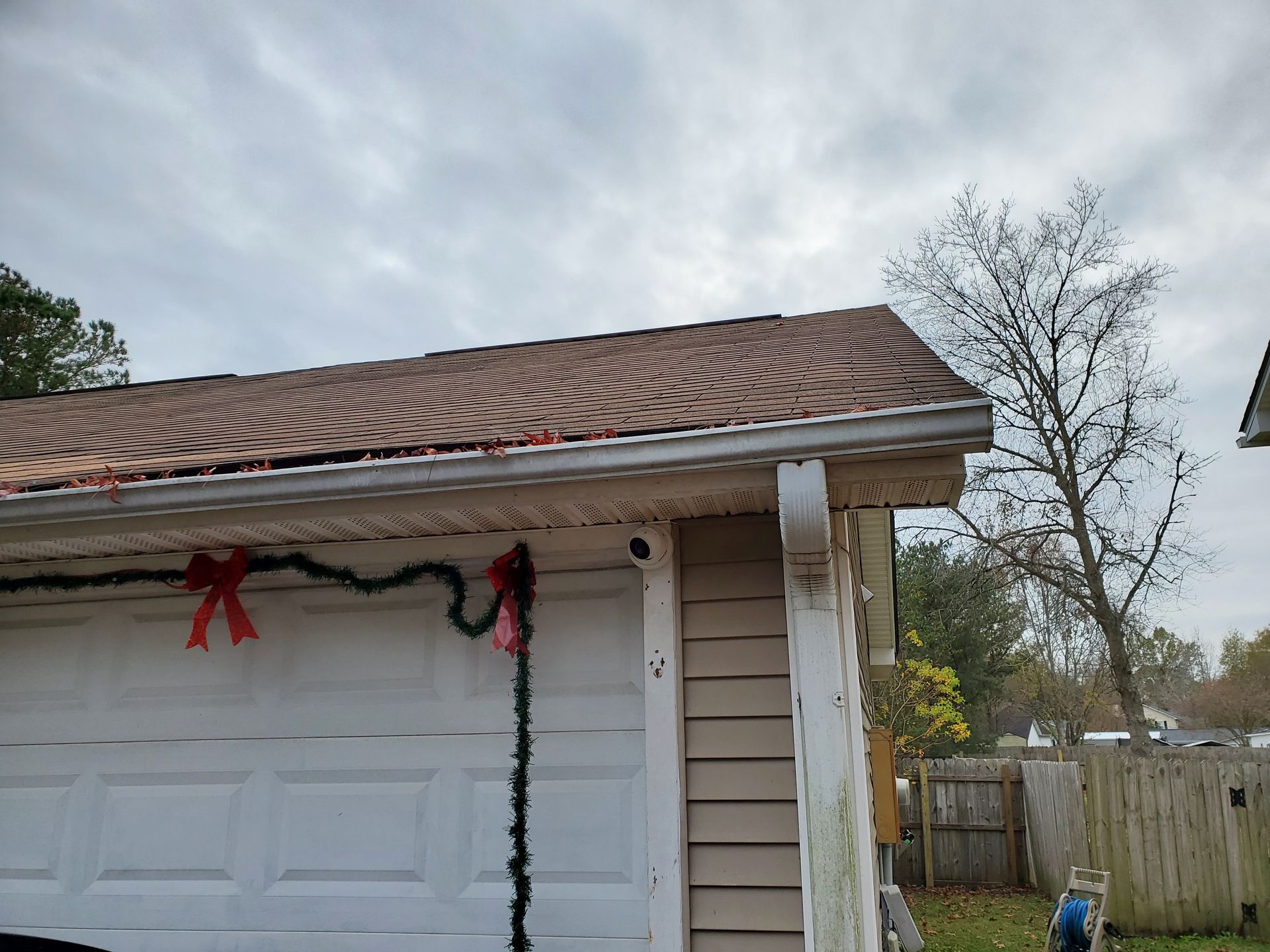 Garage with brown roof, white door, and green garland with red bows. Cloudy sky.