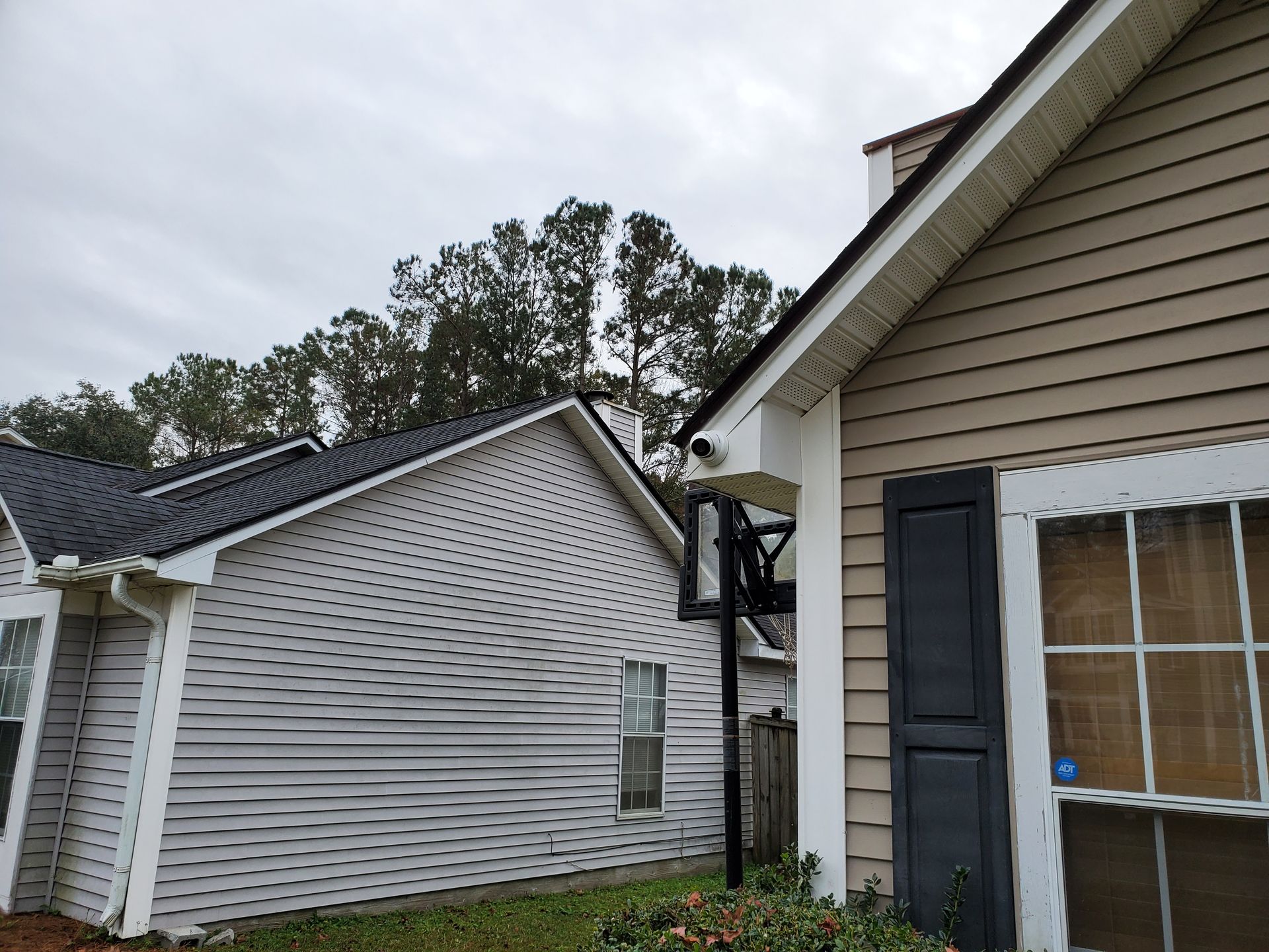 Two houses, one with a basketball hoop, and a security camera on the right house under a cloudy sky.