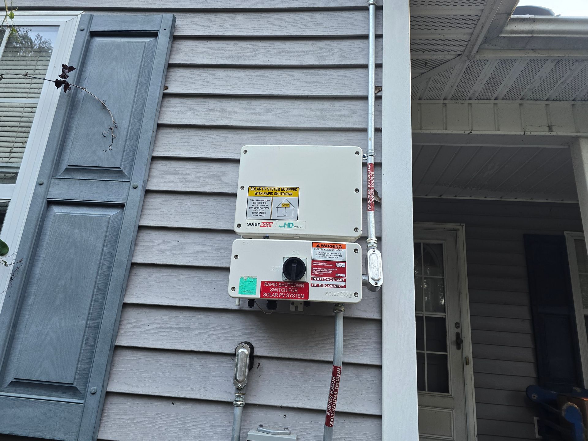 White solar inverter boxes mounted on gray house siding. Conduit runs down the side.