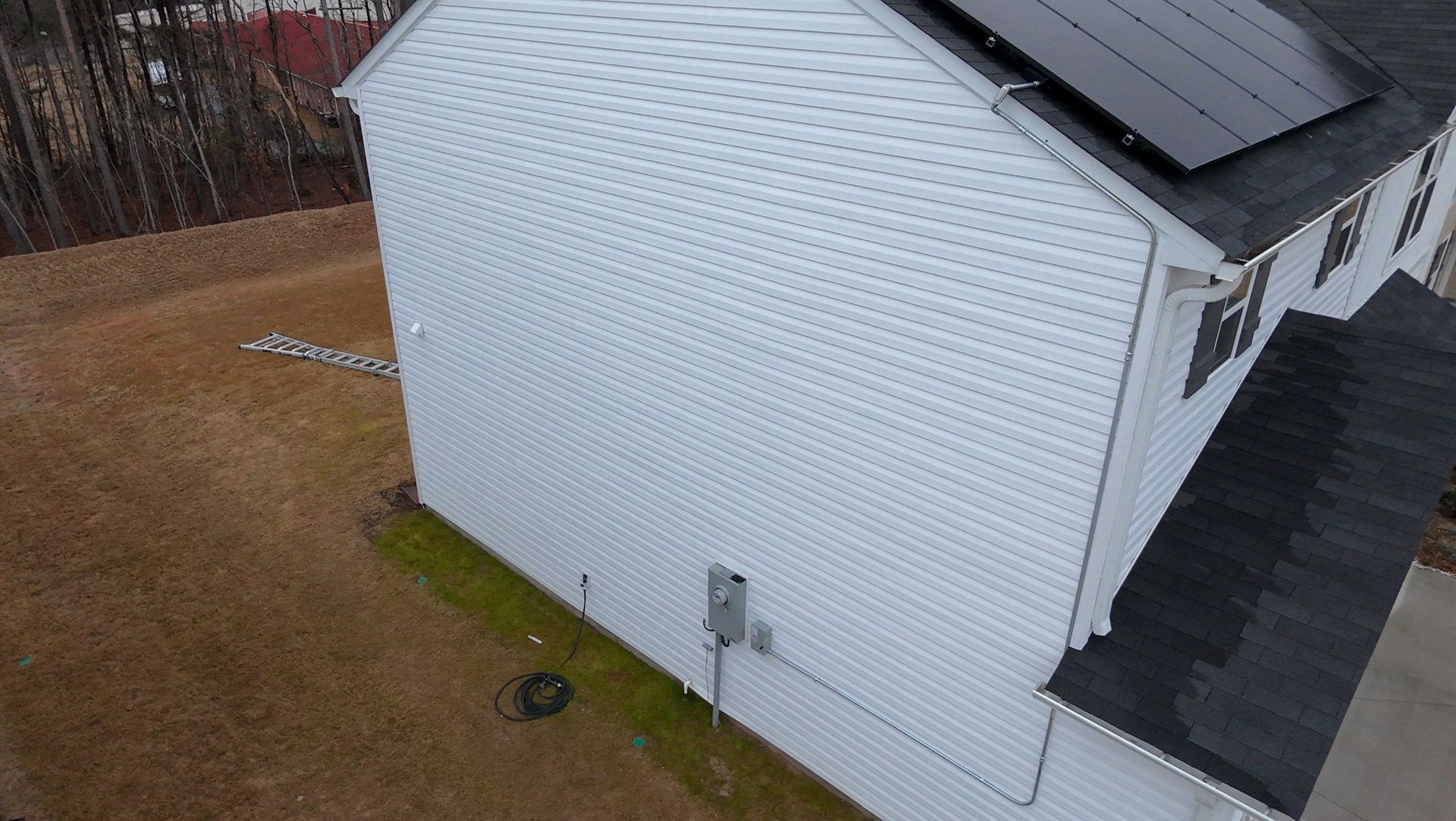 White house with black roof, solar panels, and siding, in a grassy yard.